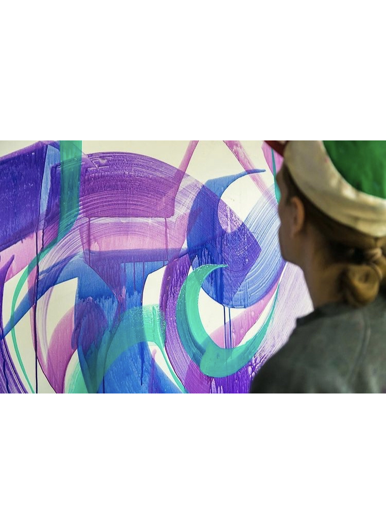 Person with a hat observes colorful abstract painting with purple, blue, green, and pink shapes.