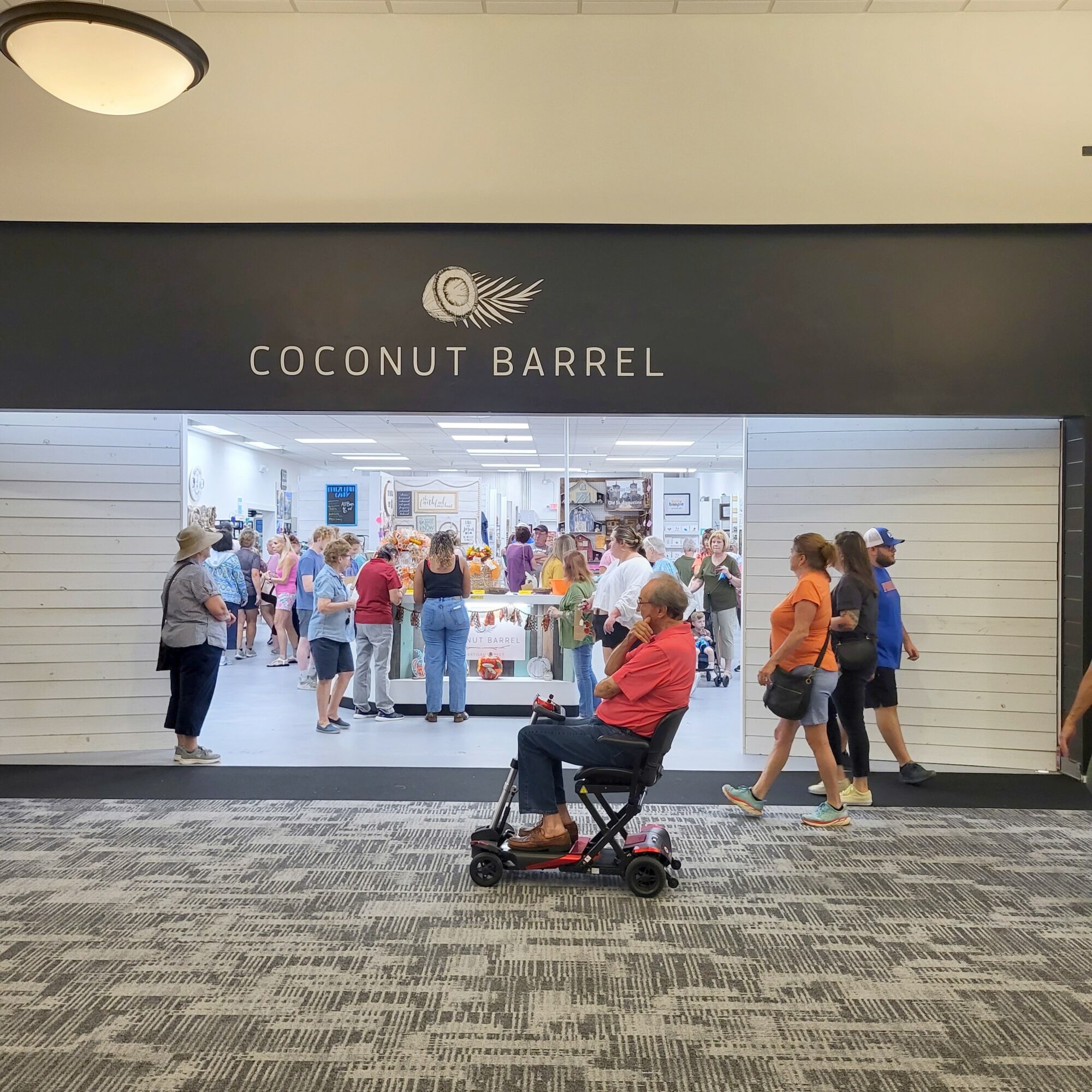 People shopping inside Coconut Barrel store, with a person in a wheelchair in front, in an indoor mall area.