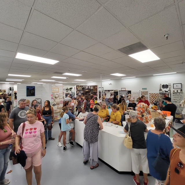 Crowd of people shopping and browsing in a store with white walls and ceiling, various displays, and a checkout counter.