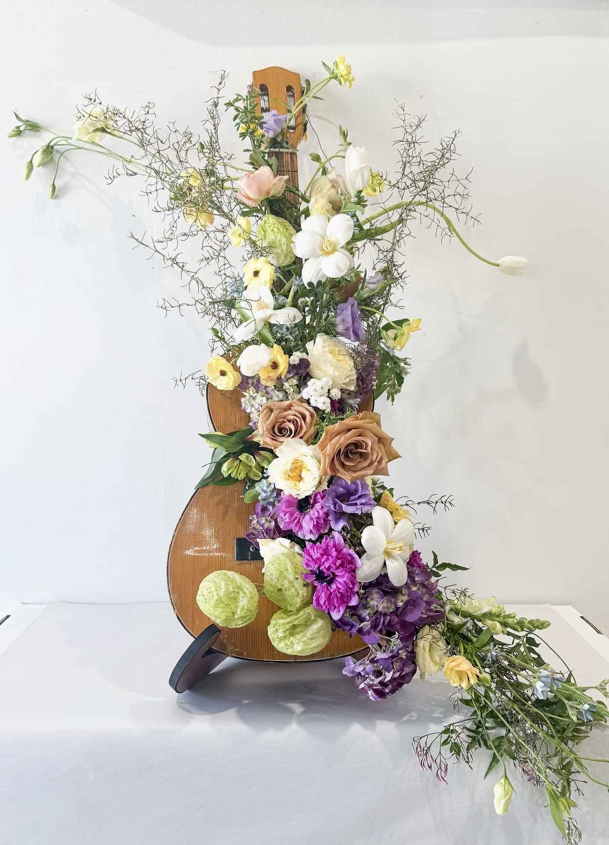 Flower arrangement with roses, orchids, and greenery in a brown vase on a white surface.