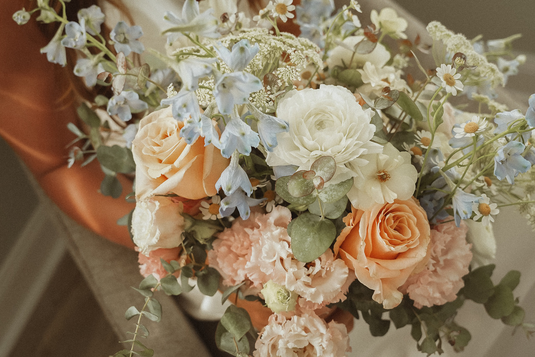 A bouquet of white, peach, and blue flowers with green leaves, arranged in a natural style.