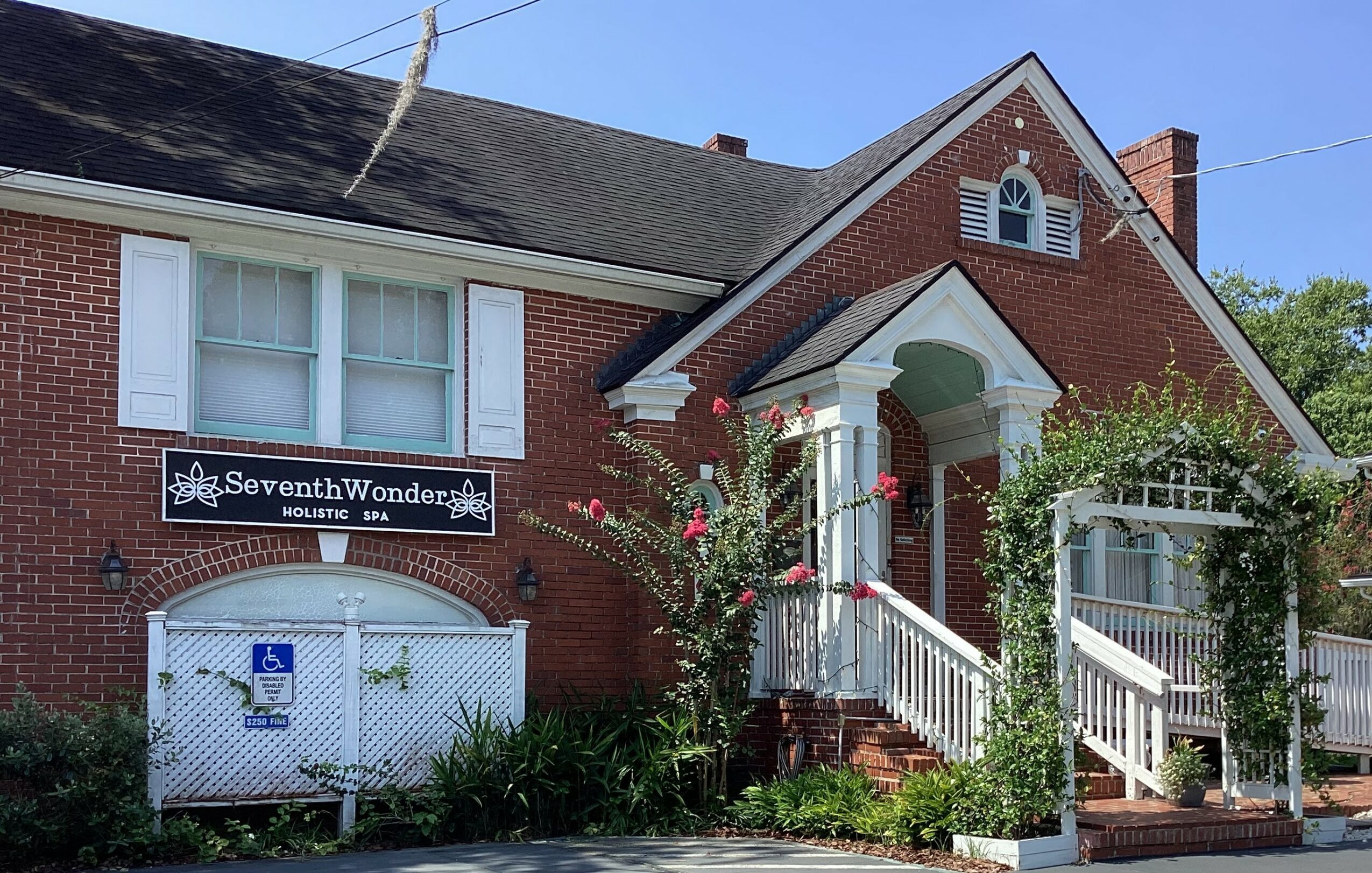 Brick building with white window shutters, a sign reading Seventh Wonder, and a staircase with white railing leading to the entrance.
