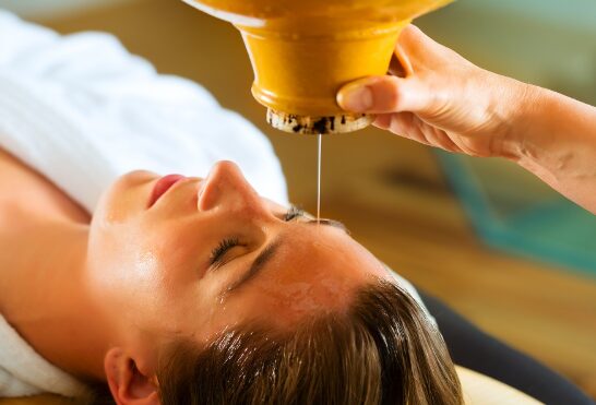 Person receiving a facial treatment with a yellow device held above their face, eyes closed, lying down.