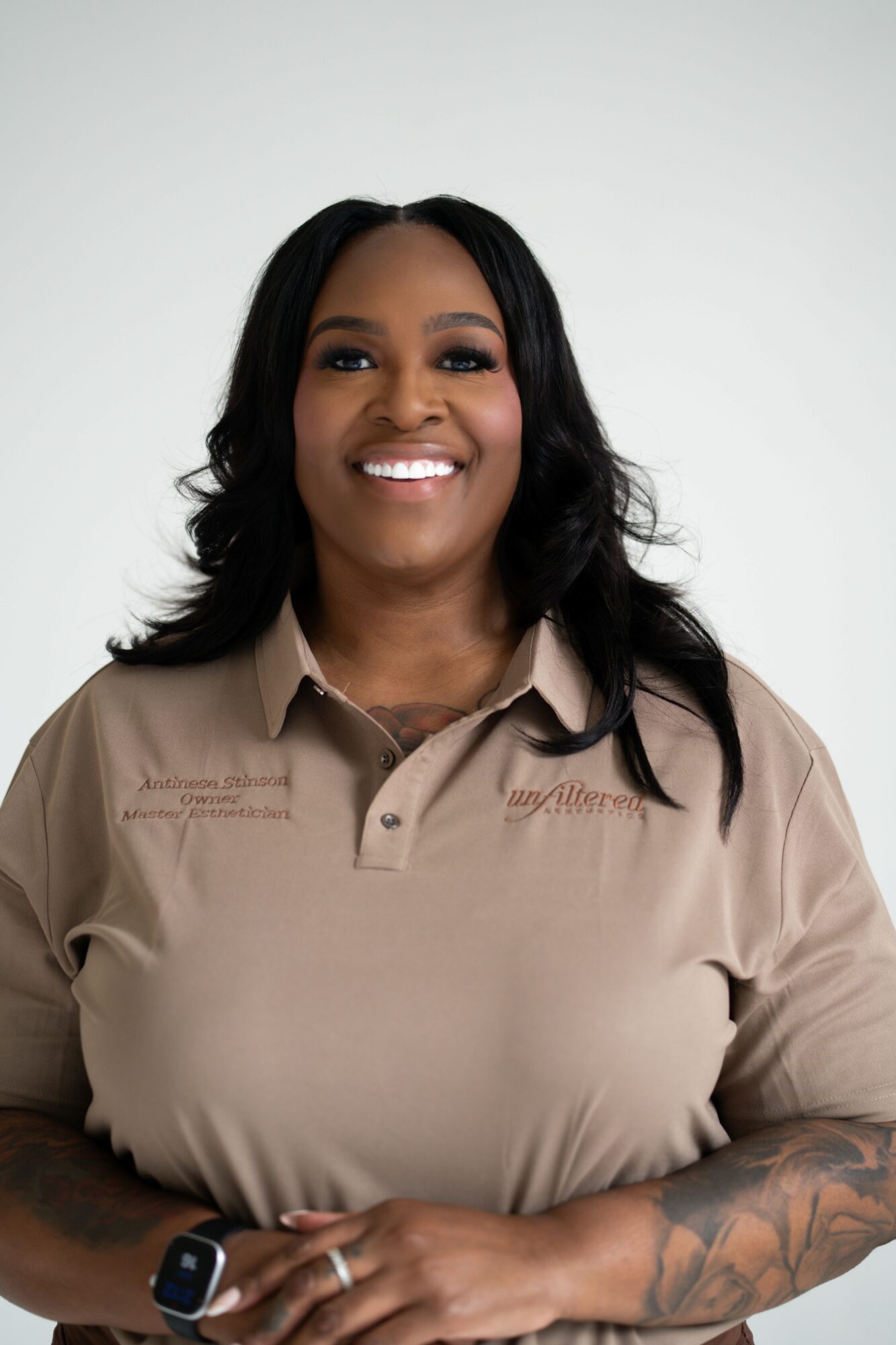 Smiling woman with long dark hair wearing a beige polo shirt, standing against a plain background.
