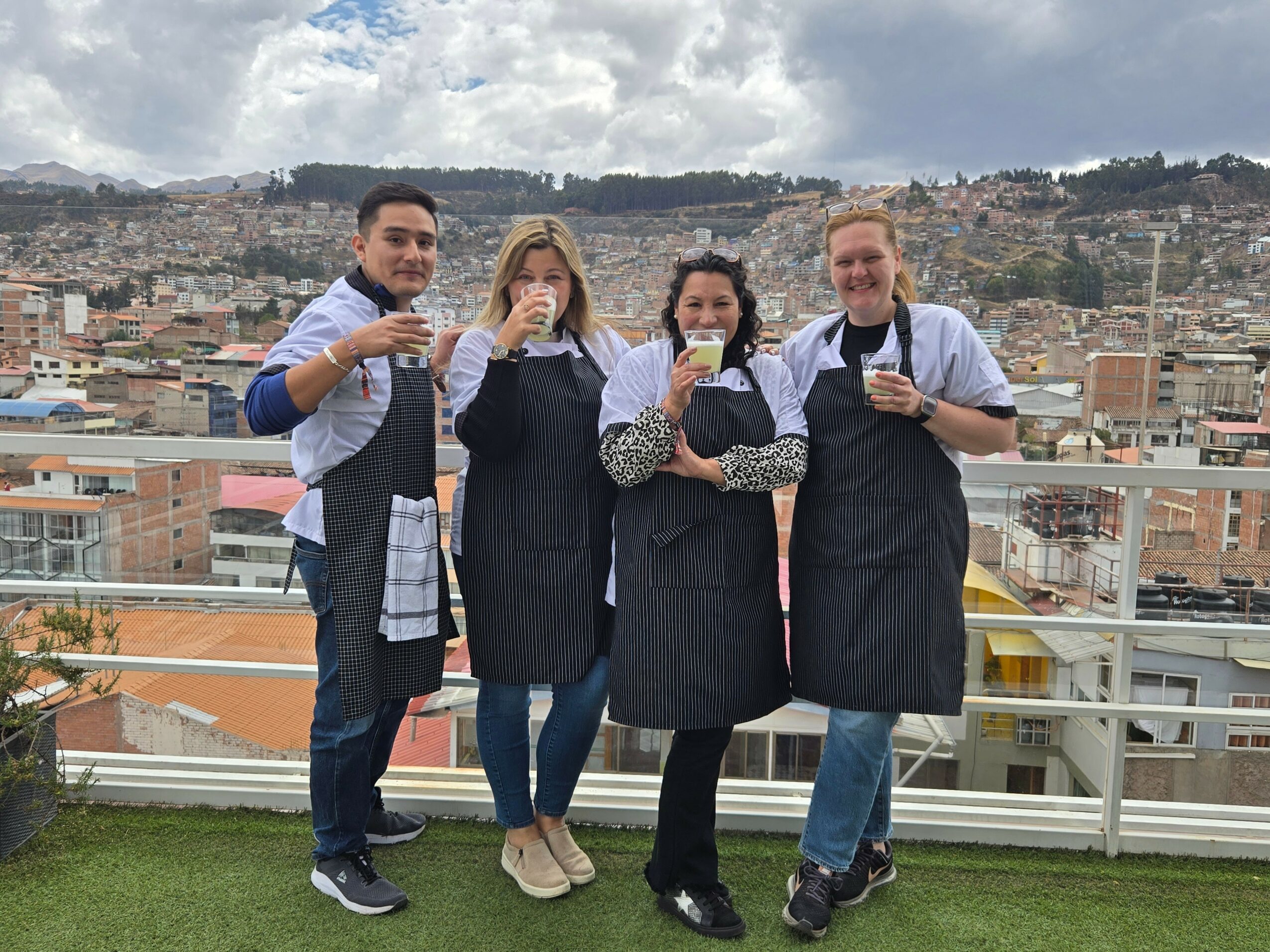 Four people standing outdoors on a rooftop, holding cups, with a cityscape in the background.
