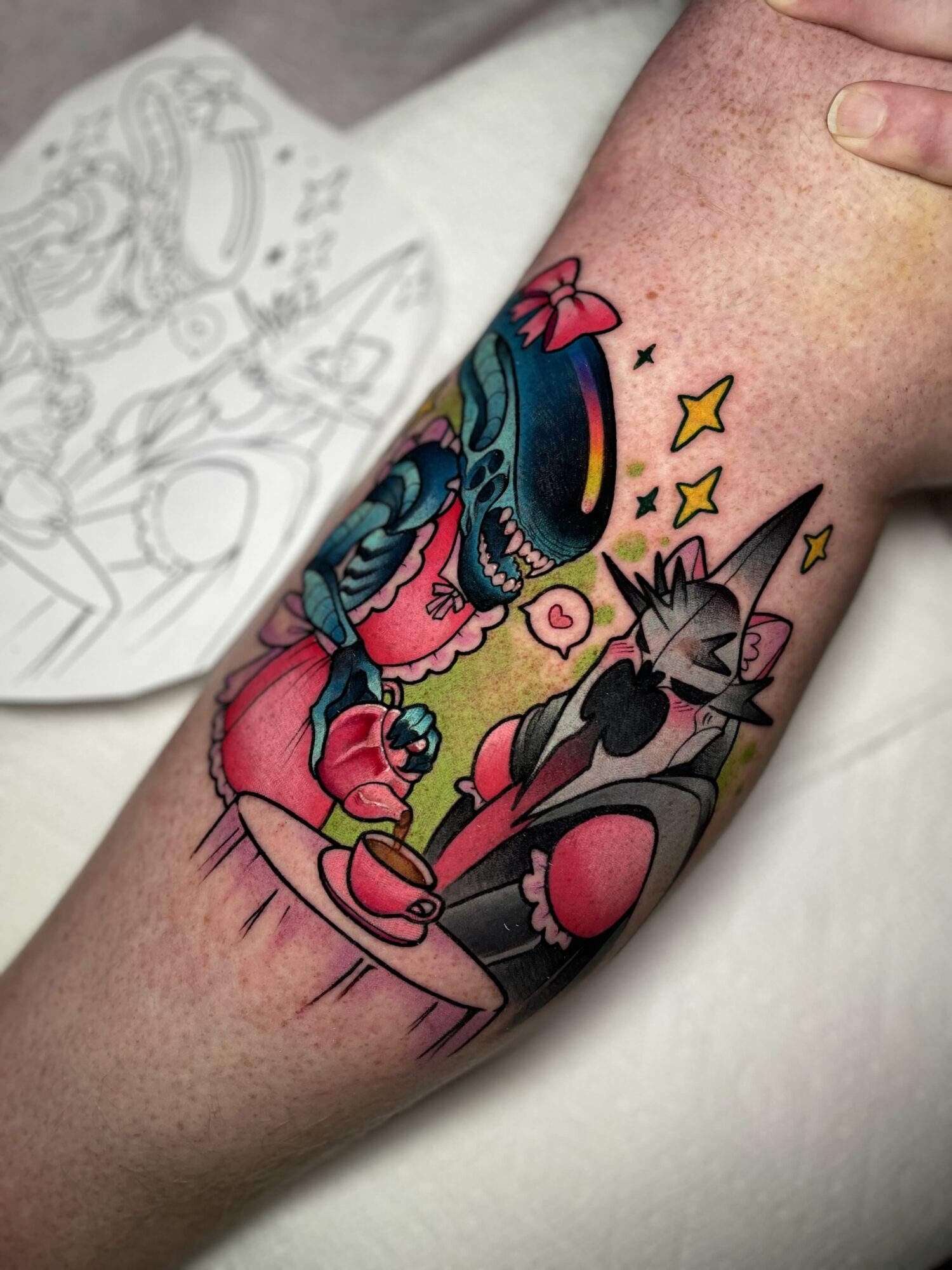 Tattoo of a girl with blue hair and a cat, both sitting on a surface with stars and a rainbow above them.