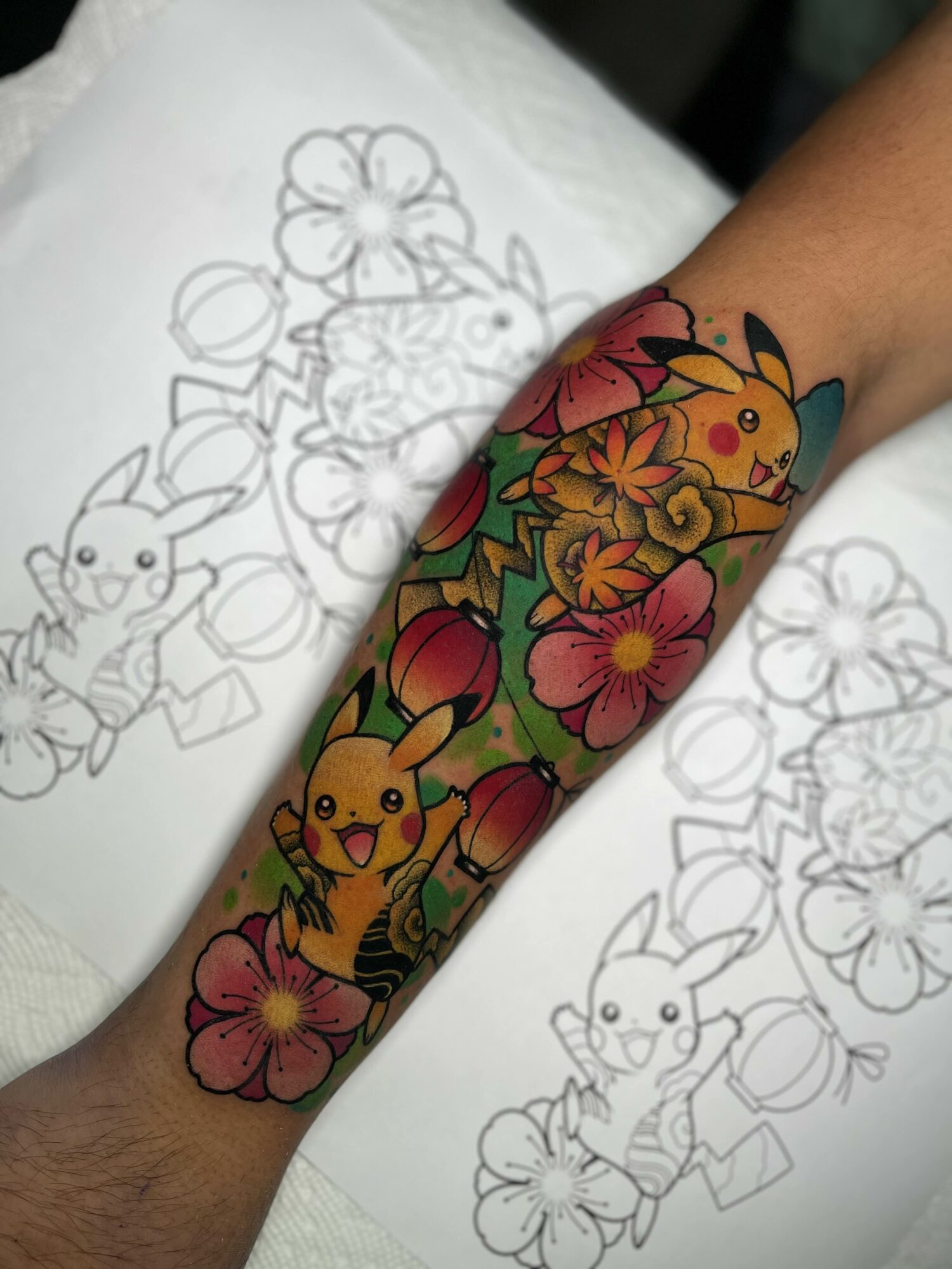 Colorful tattoo of Pikachu surrounded by pink and orange flowers on arm.