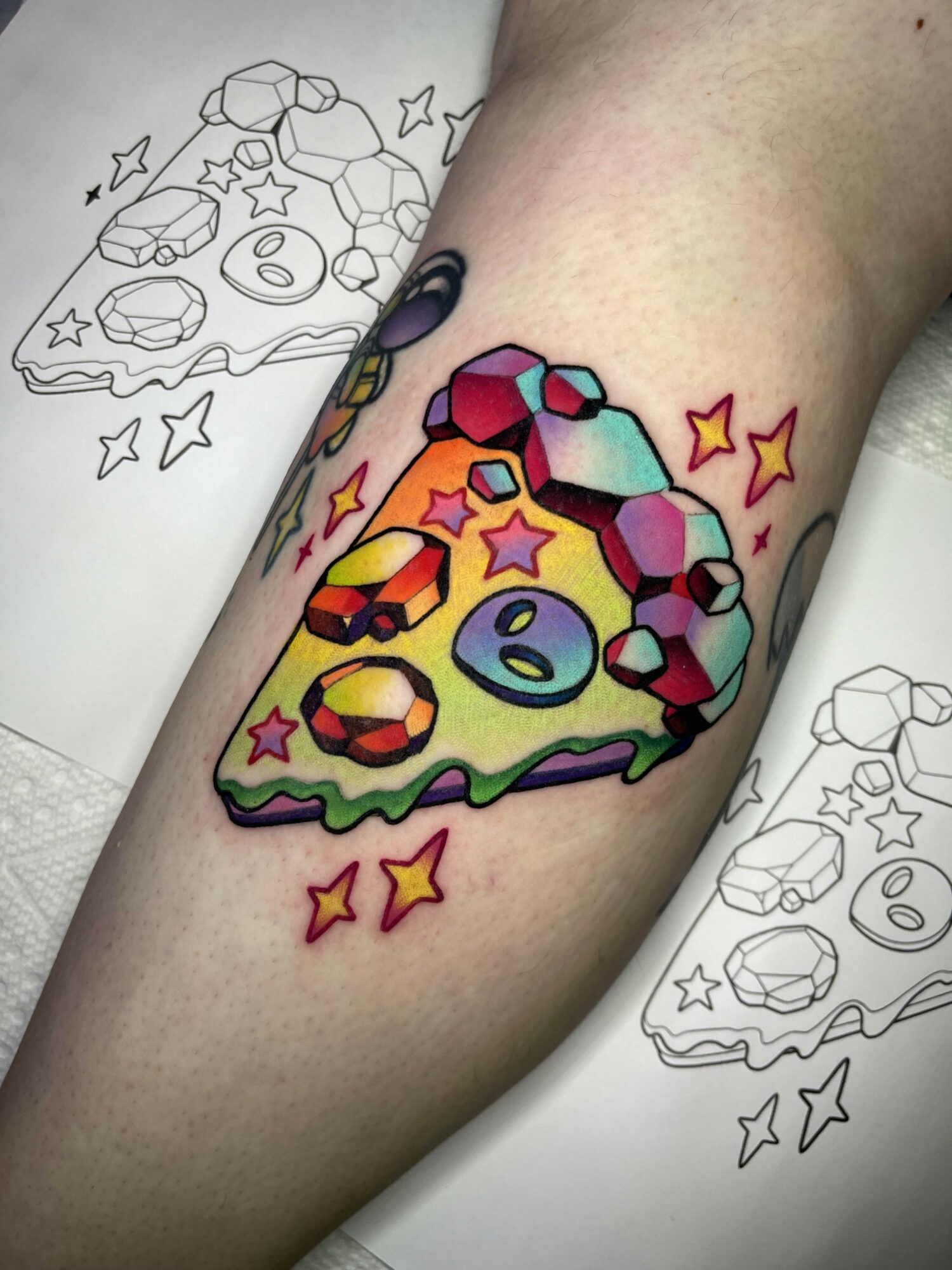 Colorful pizza slice tattoo with stars and geometric toppings on skin.