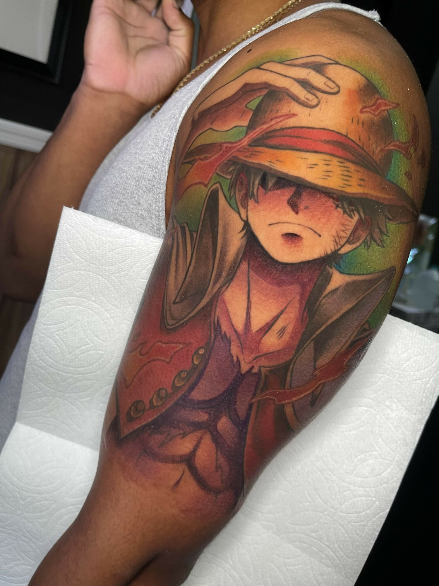 Colorful tattoo of a young girl with a straw hat, on upper arm, with vibrant background elements.