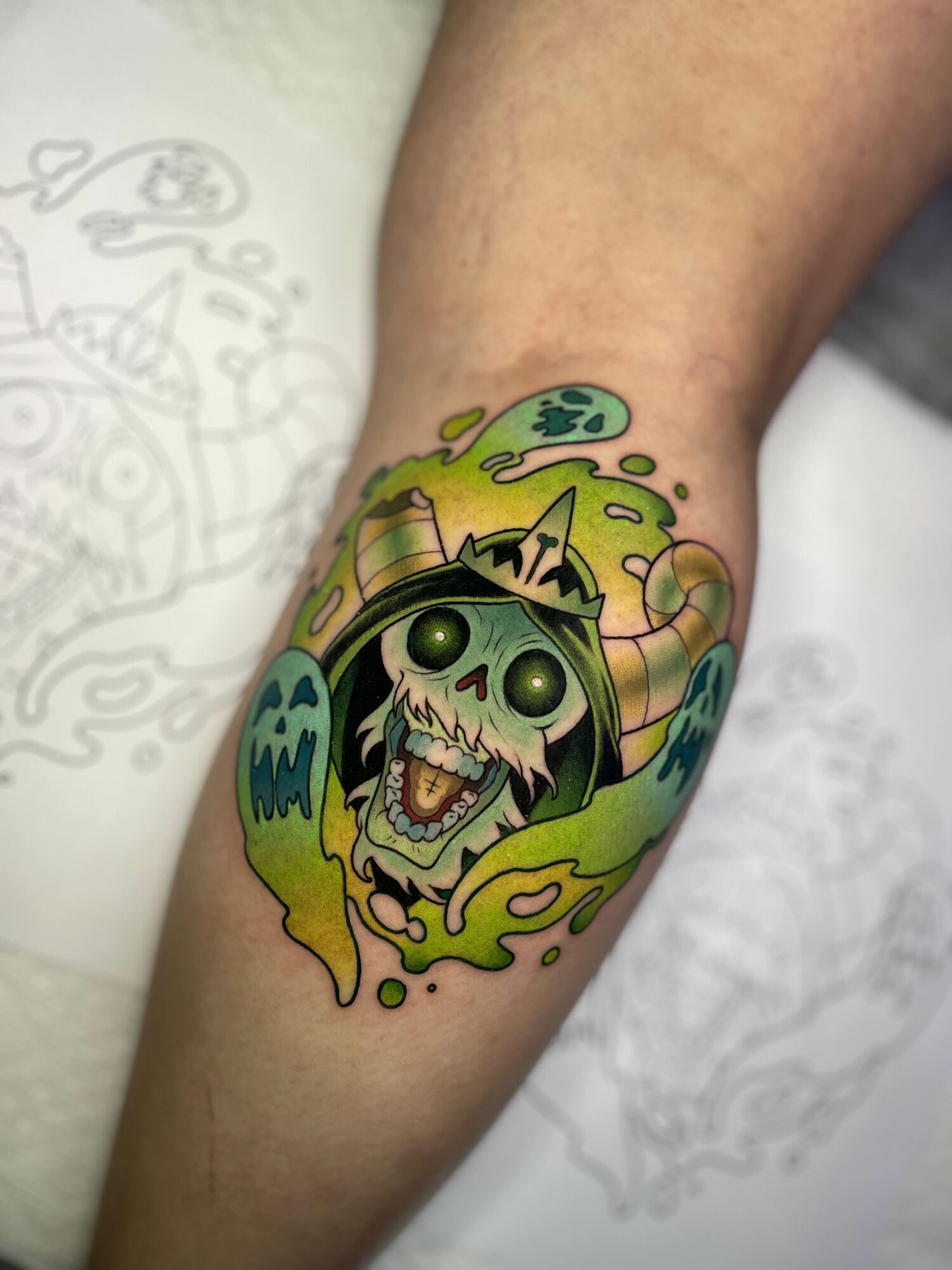 Colorful tattoo of a skull with glowing eyes, surrounded by green and yellow flames, on a person's arm.