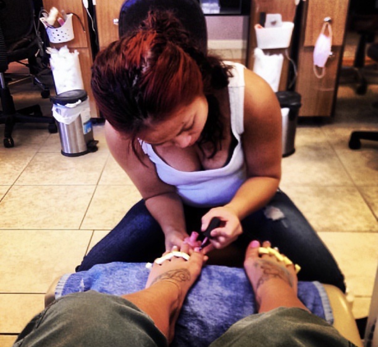 Woman receiving pedicure at salon, seated with legs extended, focusing on her toenails, salon chairs and equipment in background.
