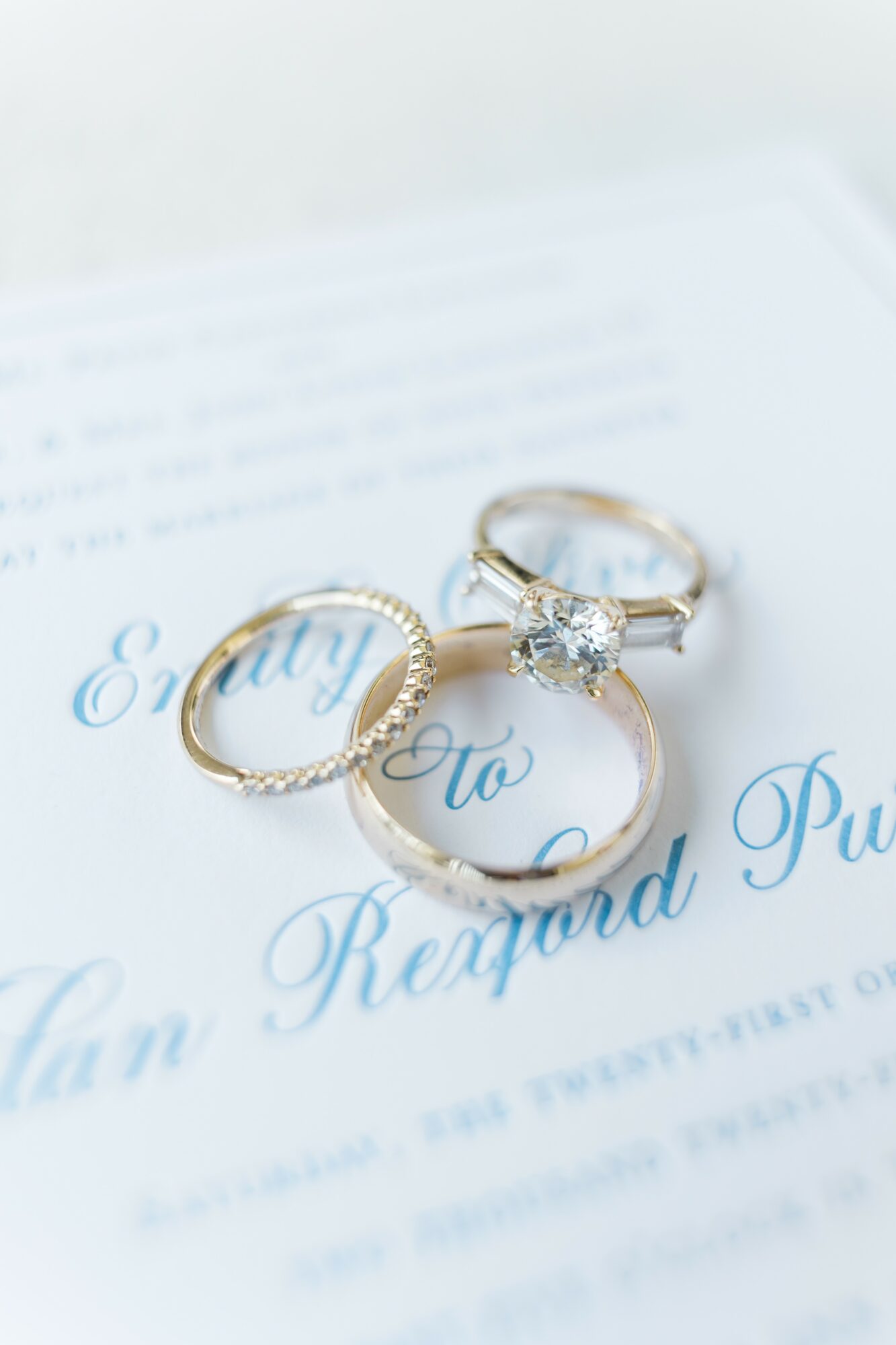 Three rings, one with a large central gemstone, placed on a document with blue cursive text, close-up view.