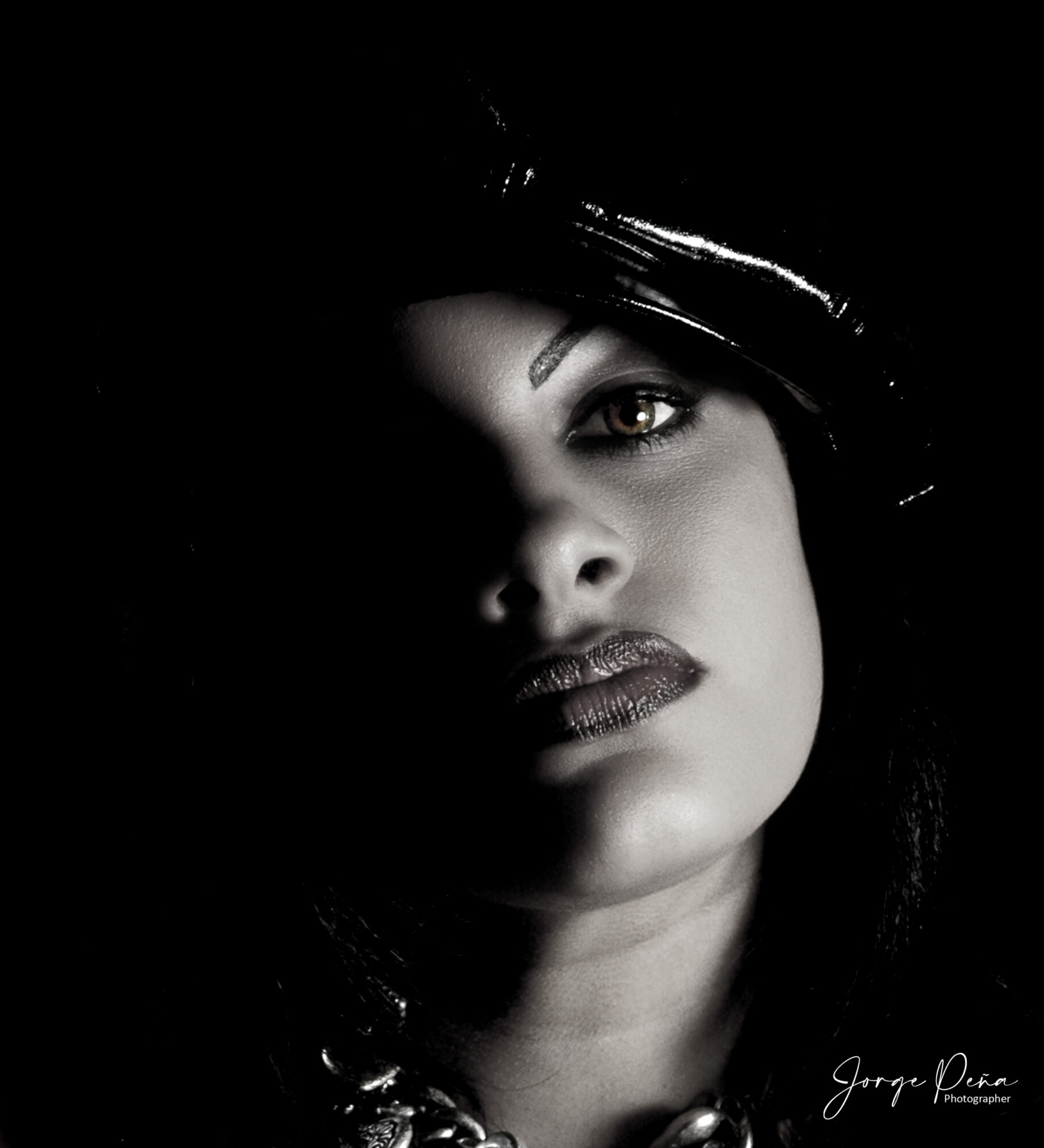 Close-up of a woman's face with dark hair, partially illuminated, showing her eye, lips, and nose, in black and white.