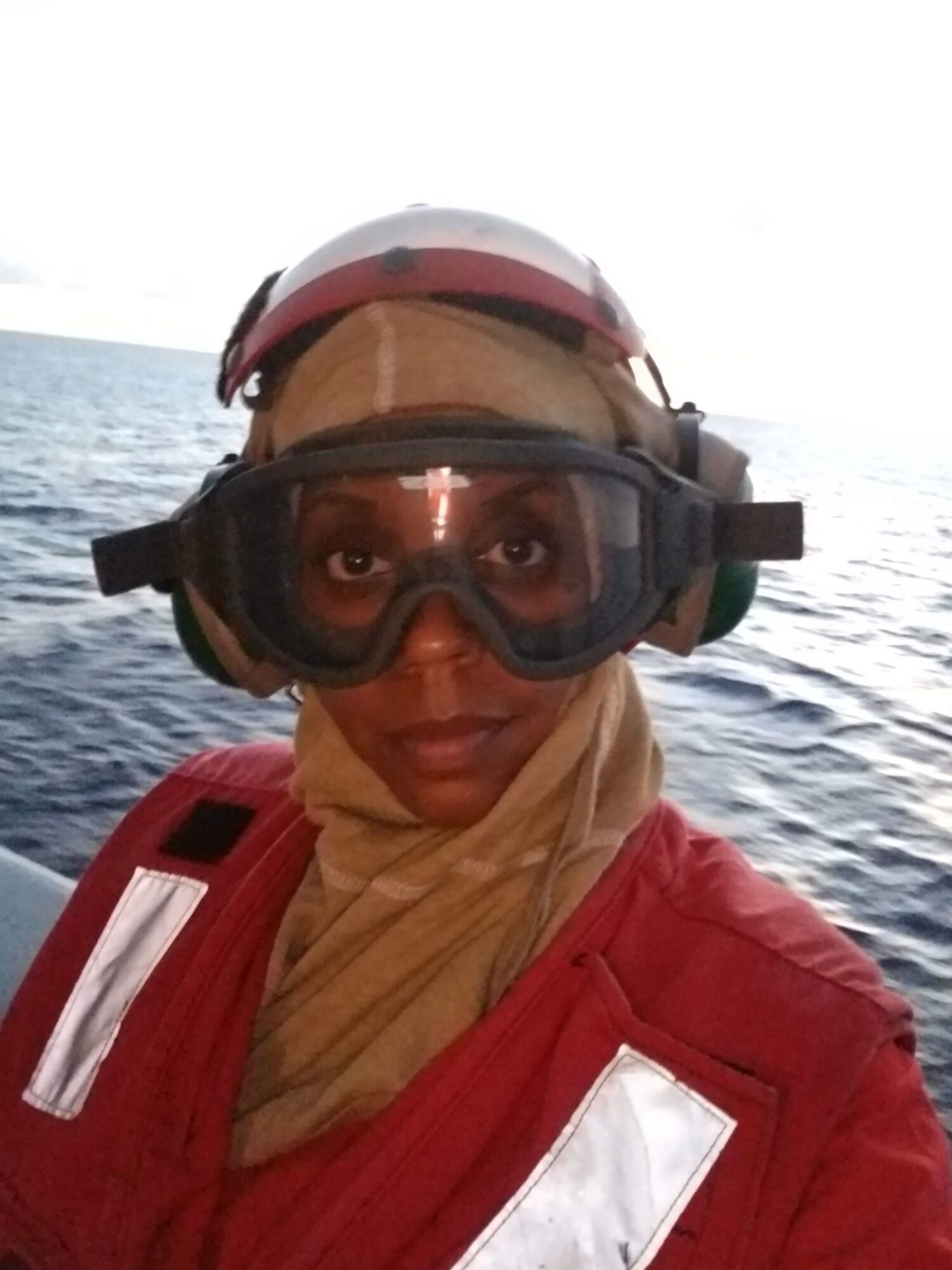 Person wearing a helmet and goggles on a boat with water in the background.
