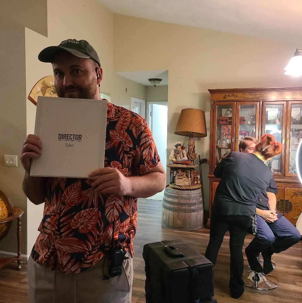 Man holding a white box with text, standing in a living room with people in the background.