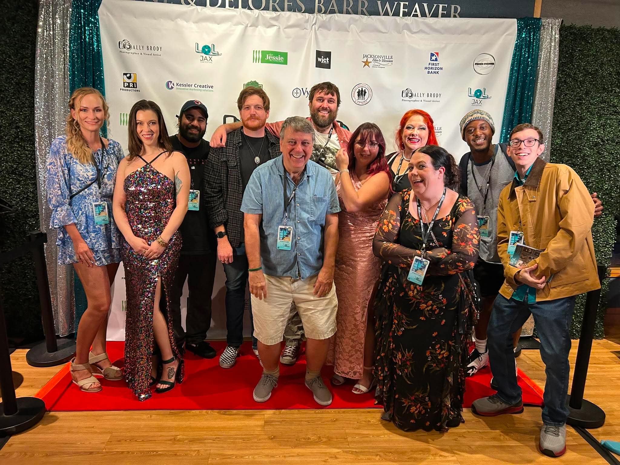 Group of eleven people standing on a red carpet in front of a backdrop, smiling for a photo, indoors.