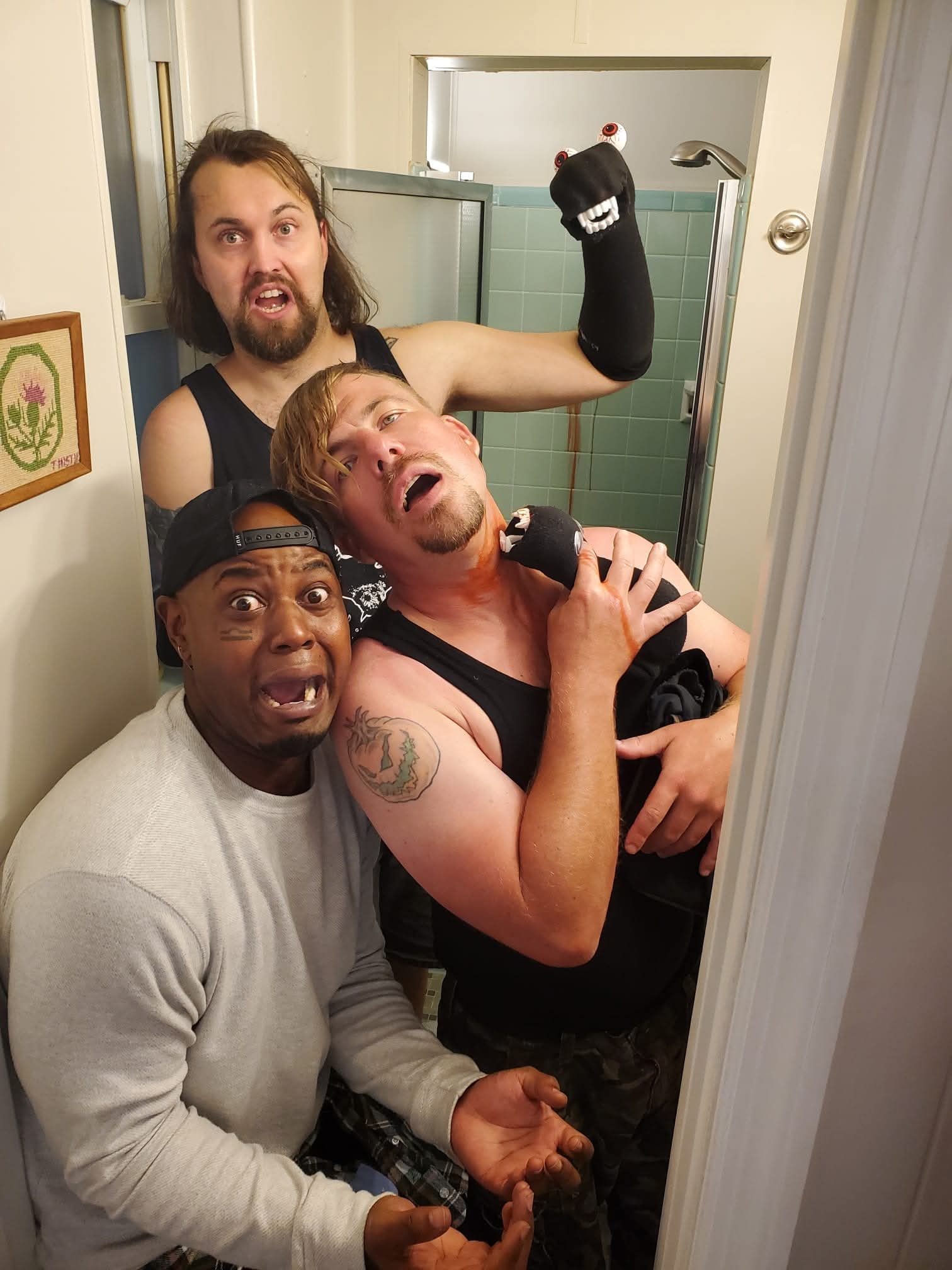 Three people in a bathroom, making surprised faces, with one holding a microphone and another wearing a cast on their arm.