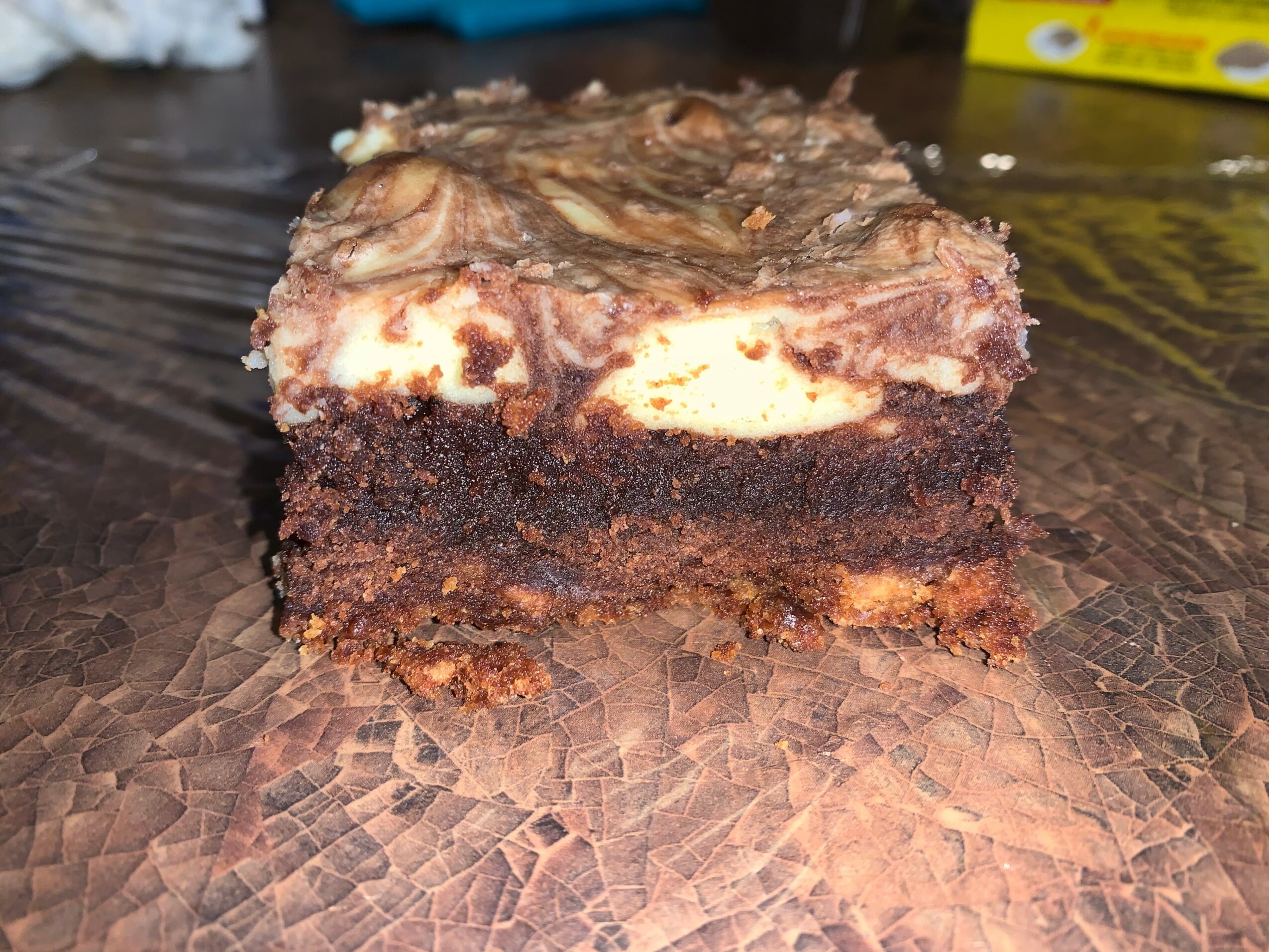 A piece of layered chocolate and cream dessert on a wooden surface, with a blurred background.