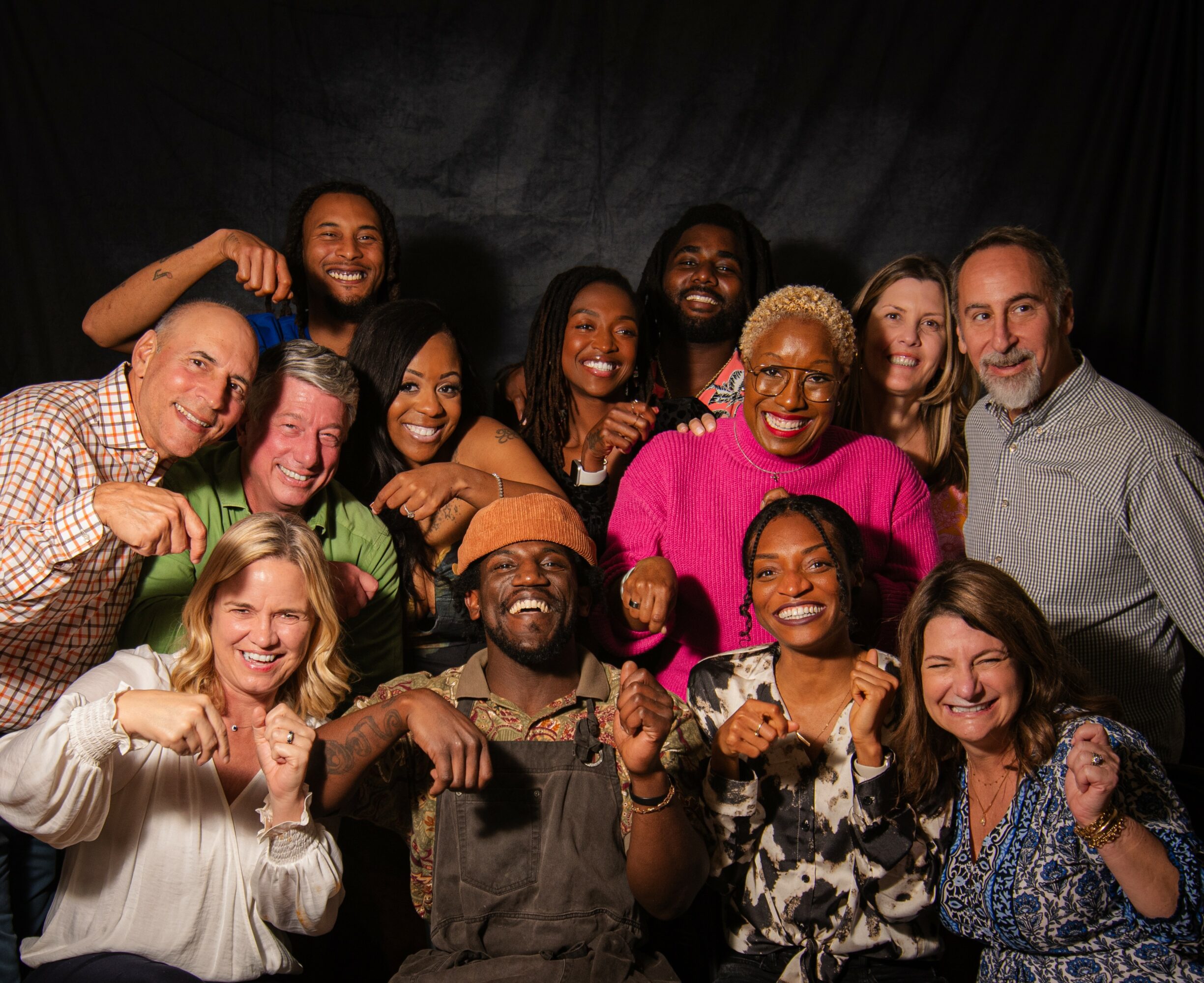 Group of diverse people smiling and posing together against a dark background.