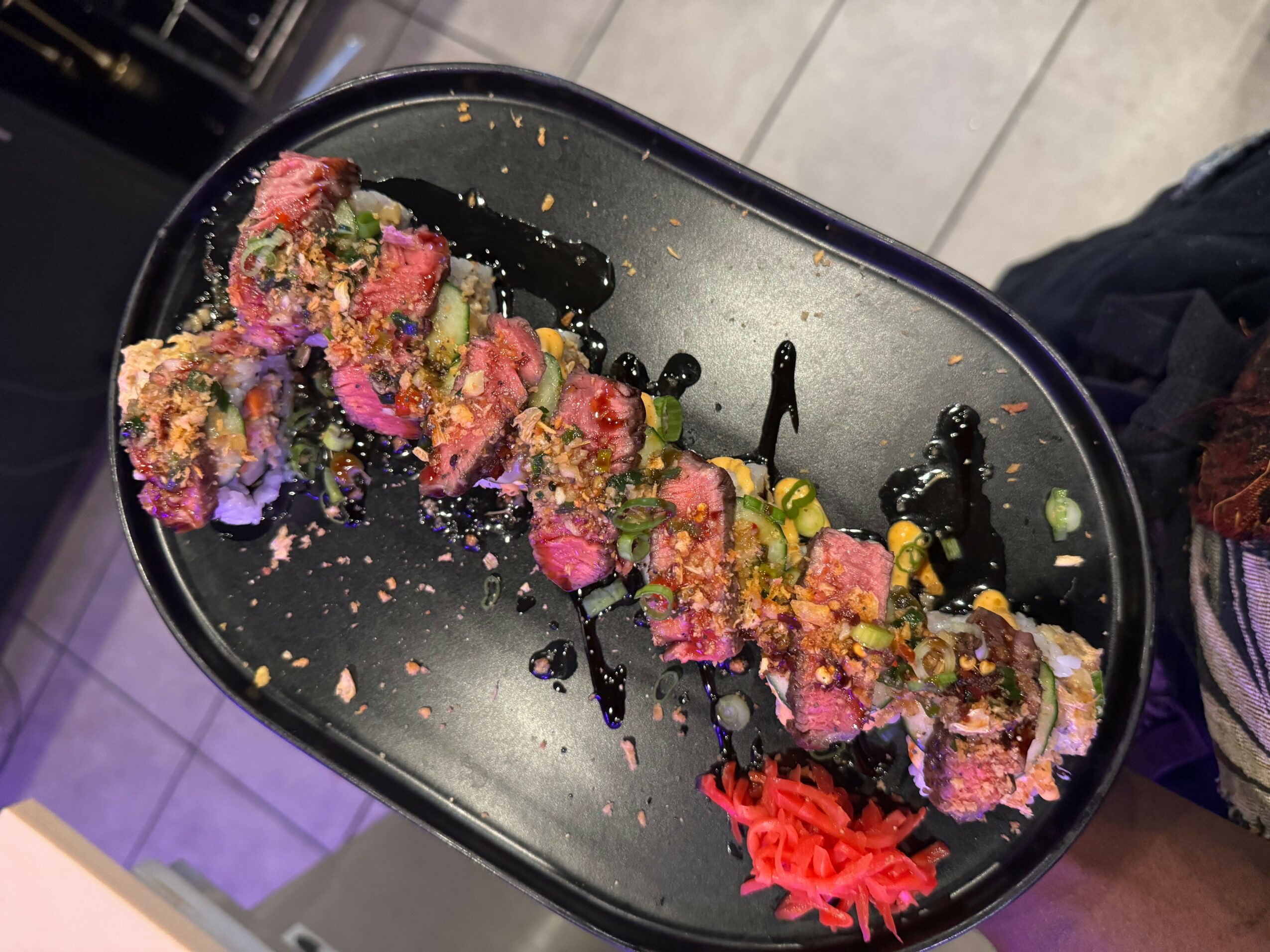 Sushi rolls with colorful toppings and a small pile of red pickled ginger on a black plate.