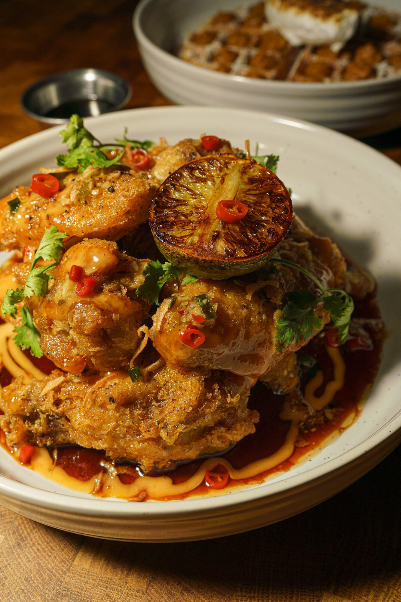 Plate with fried chicken, garnished with cilantro, red chili, and a grilled lime half, on a wooden table.