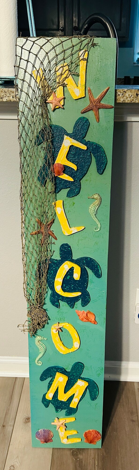 Vertical sign with colorful letters spelling 'WELCOME' and decorative elements like a starfish and plants.