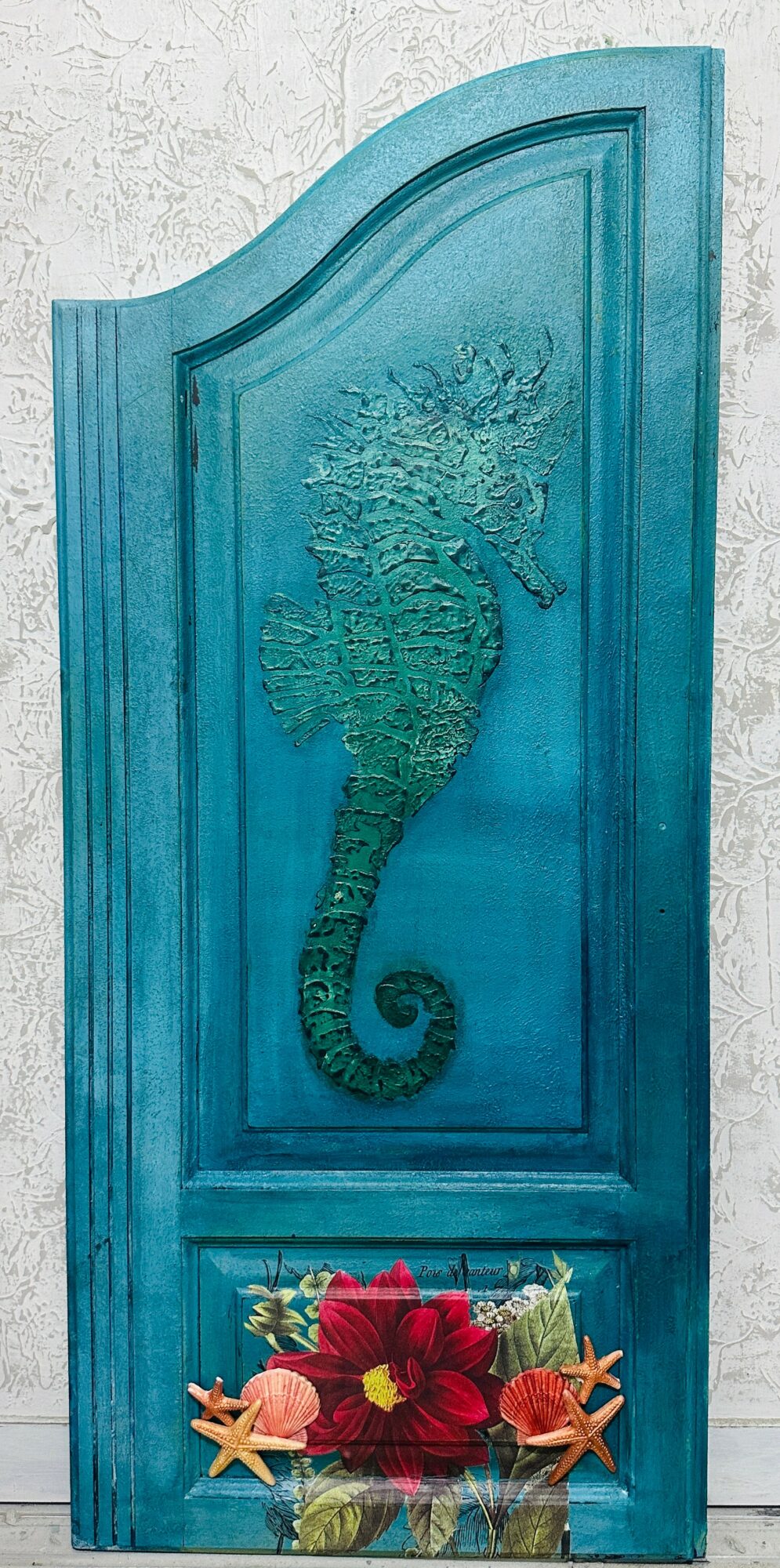 Blue door with a seahorse design and a flower arrangement at the bottom.