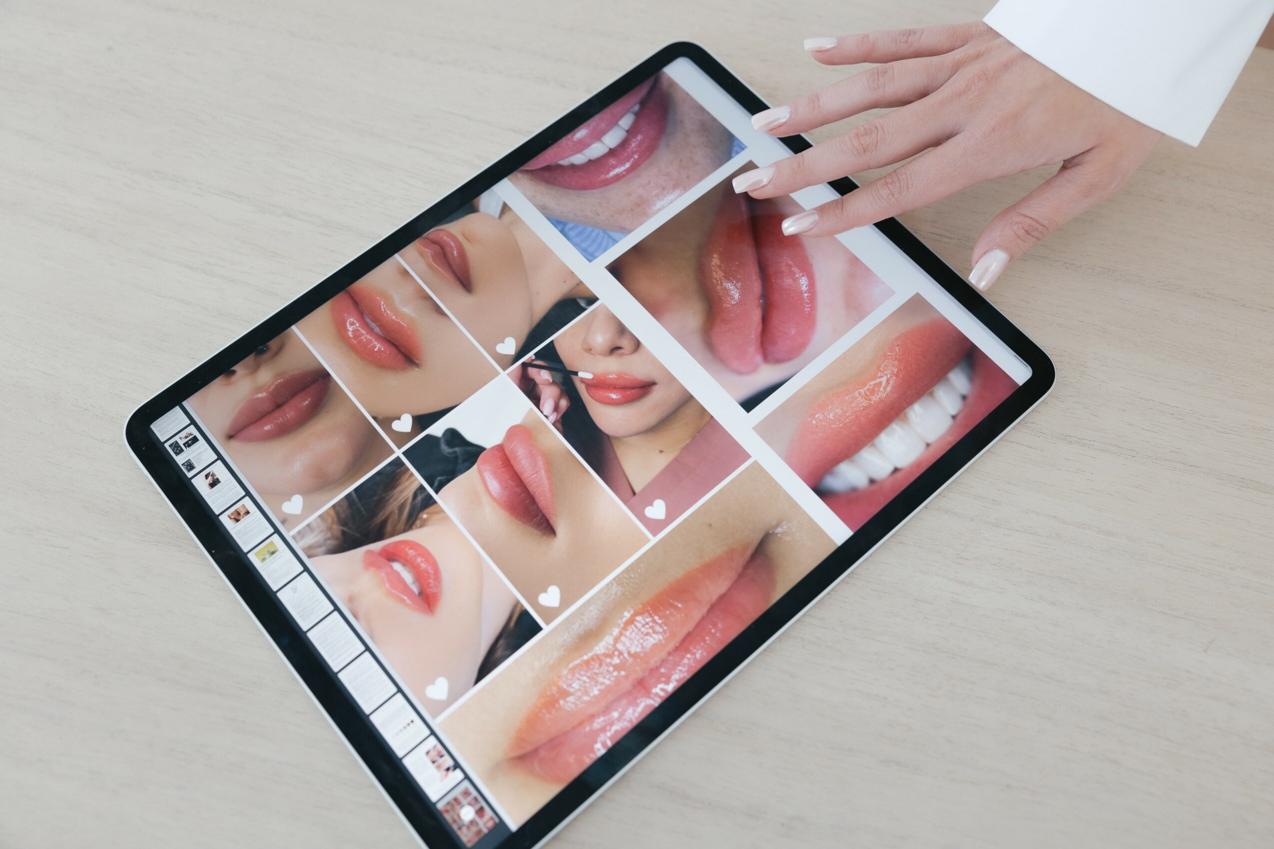 Person's hand touching a tablet displaying close-up images of lips and tongue, on a light wooden surface.
