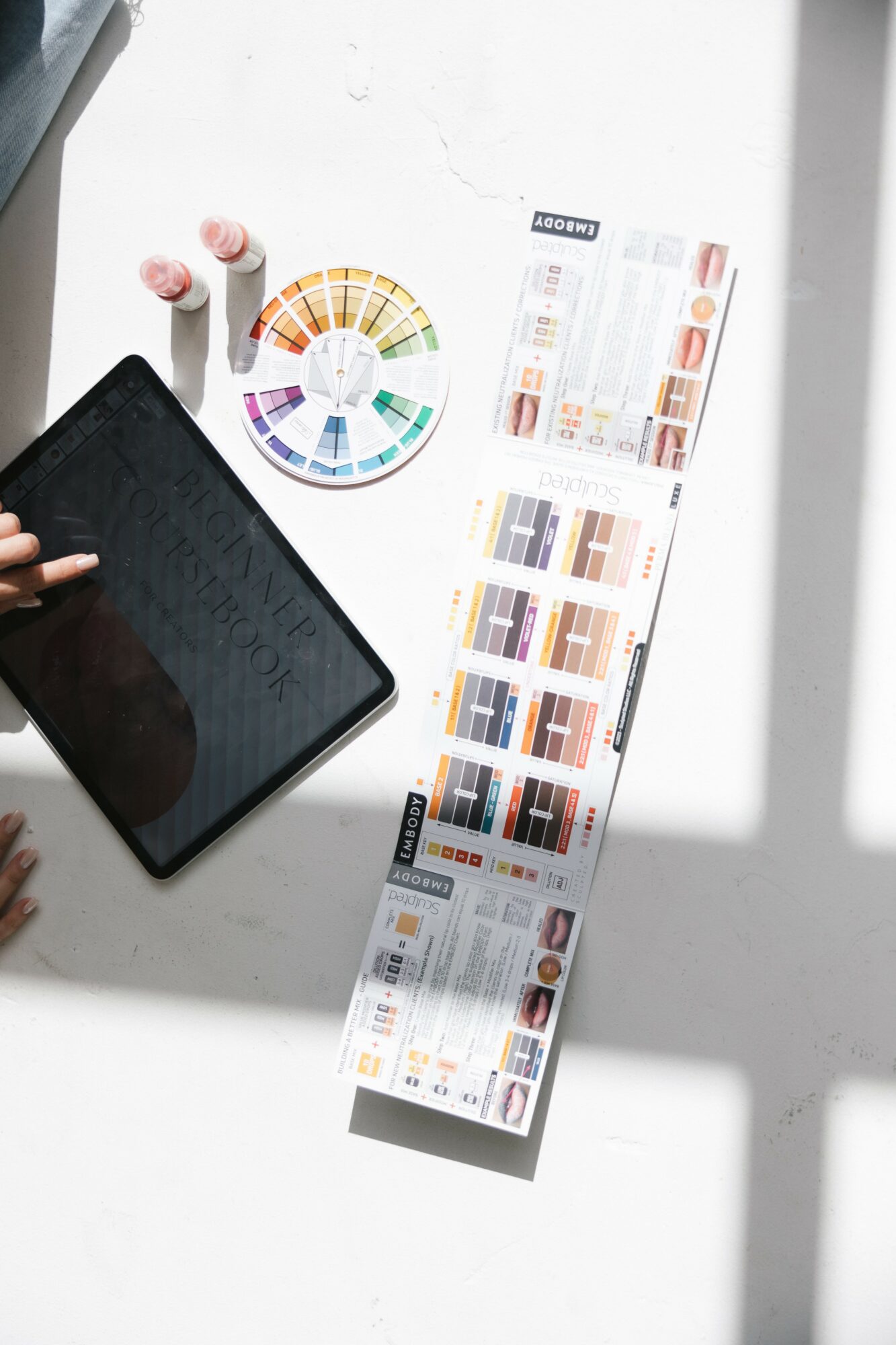 Person holding a tablet with color swatches and a color wheel on a white surface, with shadows cast on the table.