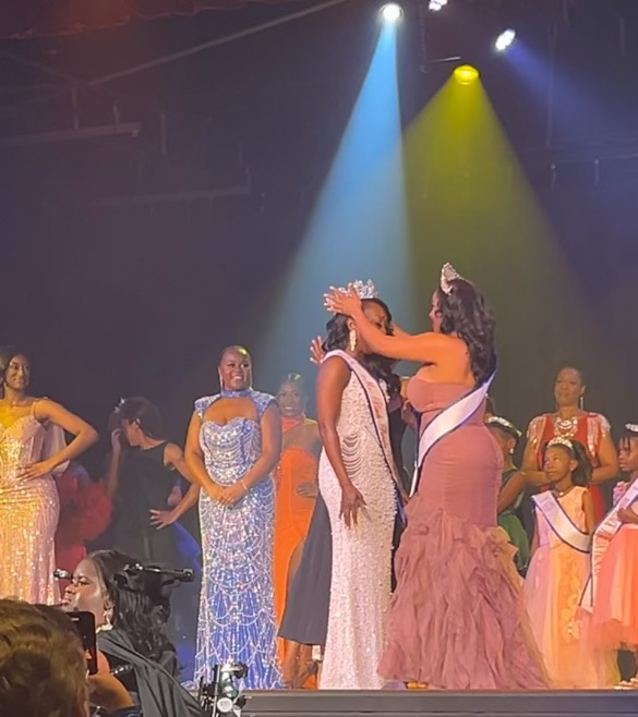 Group of women and girls on stage, some in colorful dresses, with stage lights shining down, celebrating or performing.