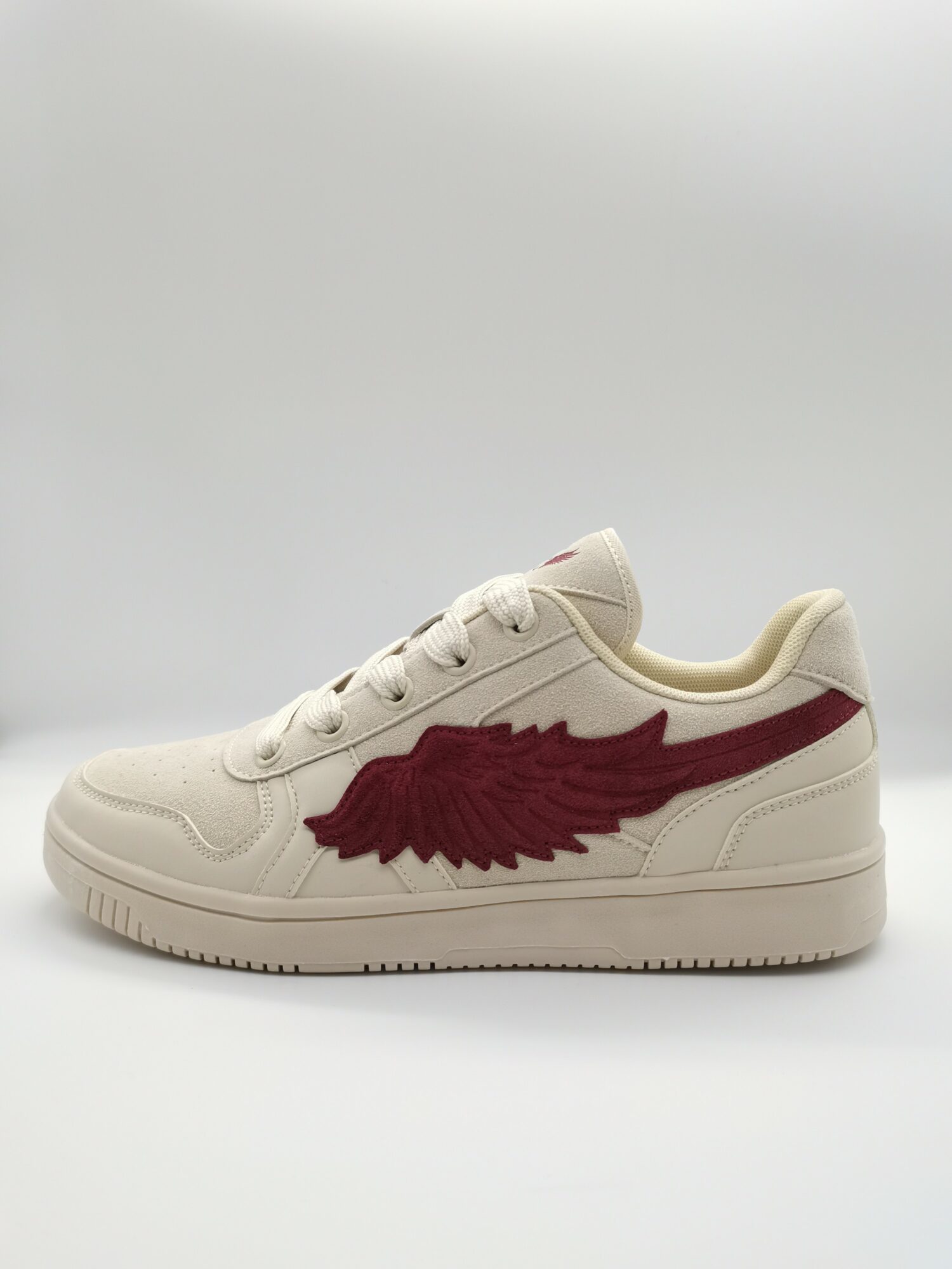Cream-colored sneaker with a large red wing logo on the side, against a plain background.