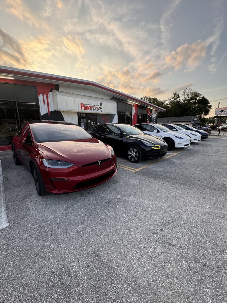 Five cars parked in front of a building during sunset, with a partly cloudy sky and trees in the background.
