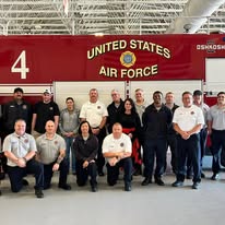 Group of people standing in front of a United States Air Force sign, some kneeling, some standing, in an indoor setting.