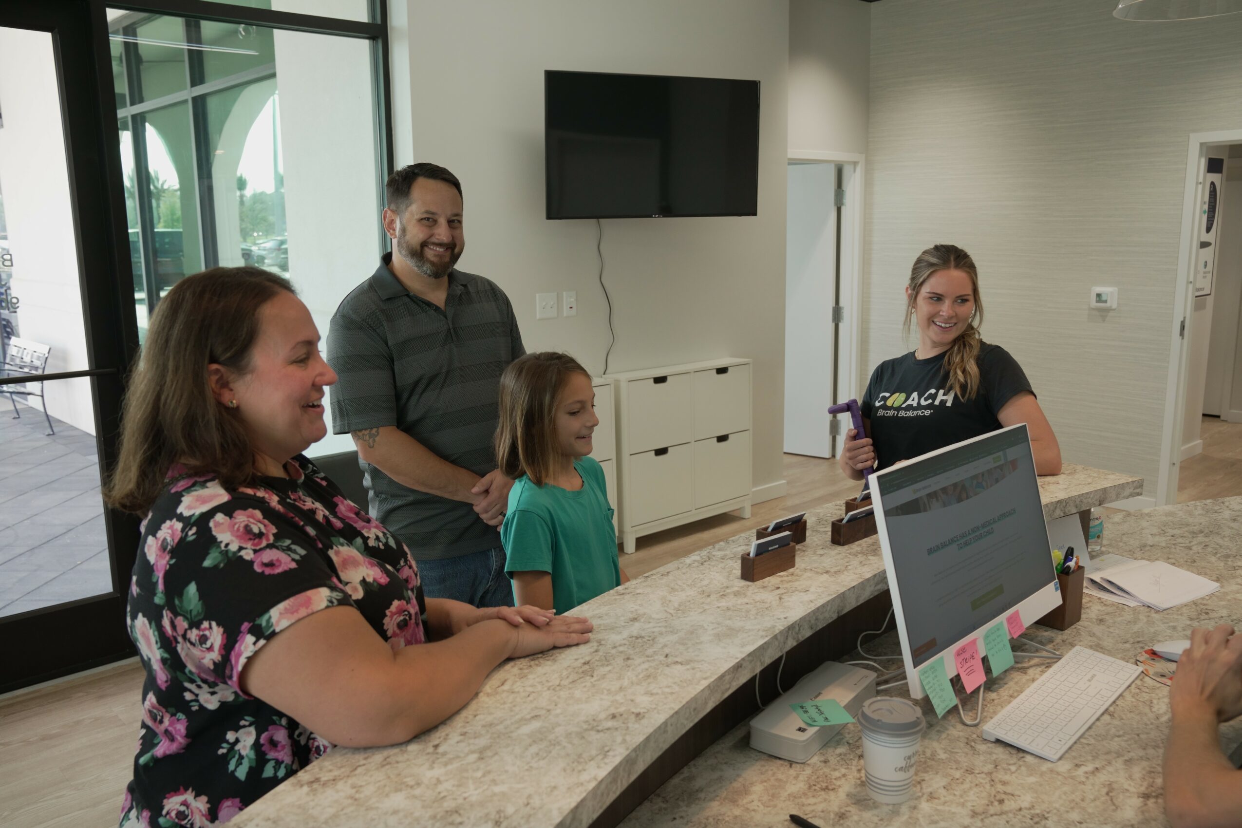 Four people, including a woman, a man, and two girls, are gathered around a curved counter in a room with large windows and a TV.