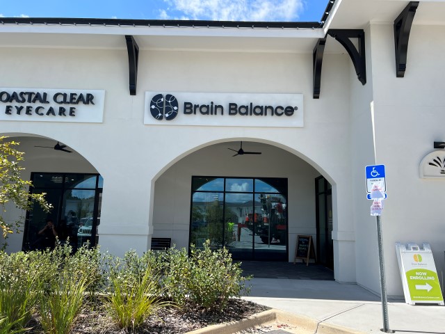 Storefront with signs for Coastal Clear Eyecare and Brain Balance, entrance with glass doors, plants in front, and a handicap parking sign.