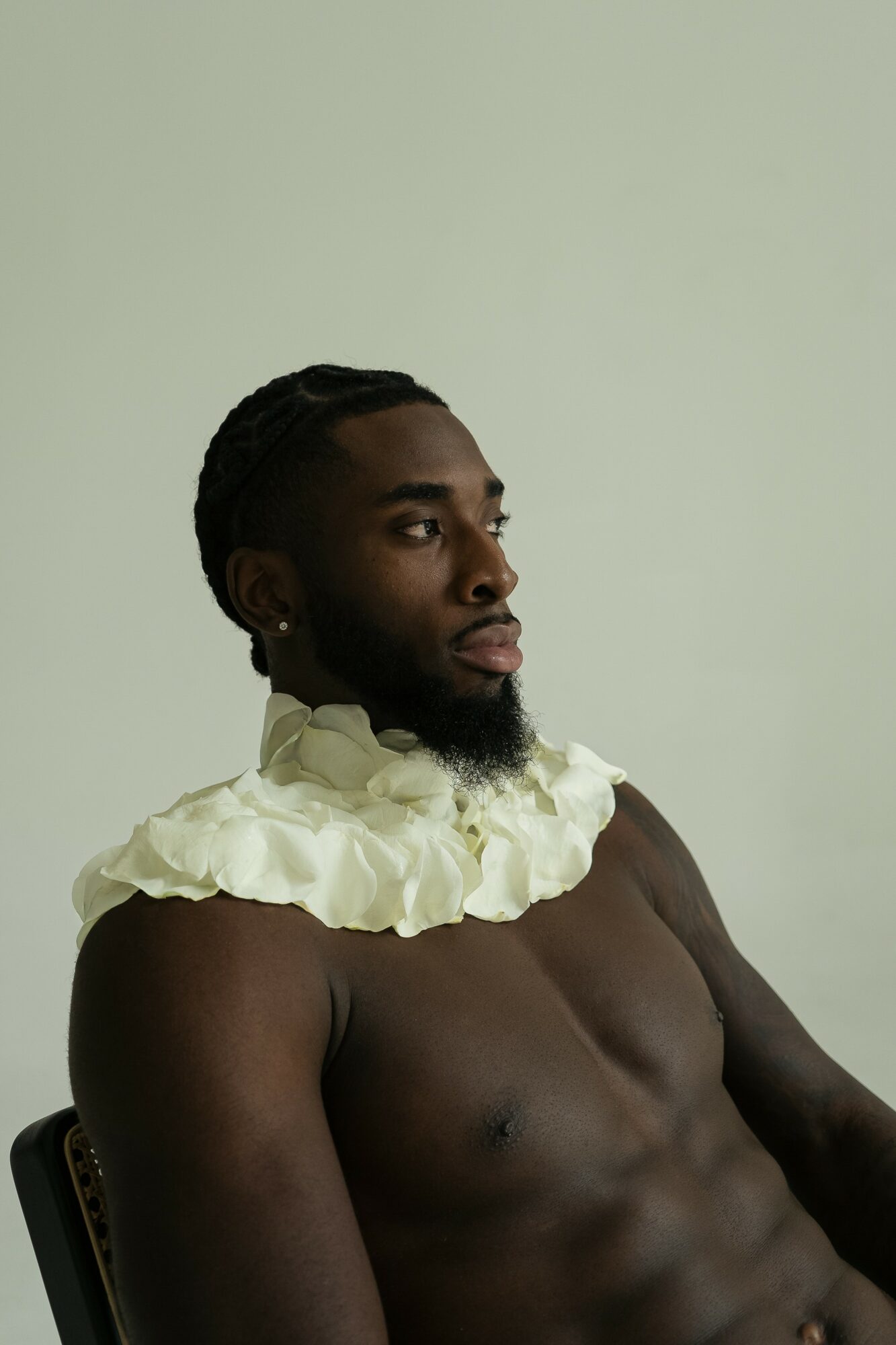 A shirtless person with a ruffled cream-colored collar around their neck, looking to the side against a plain background.