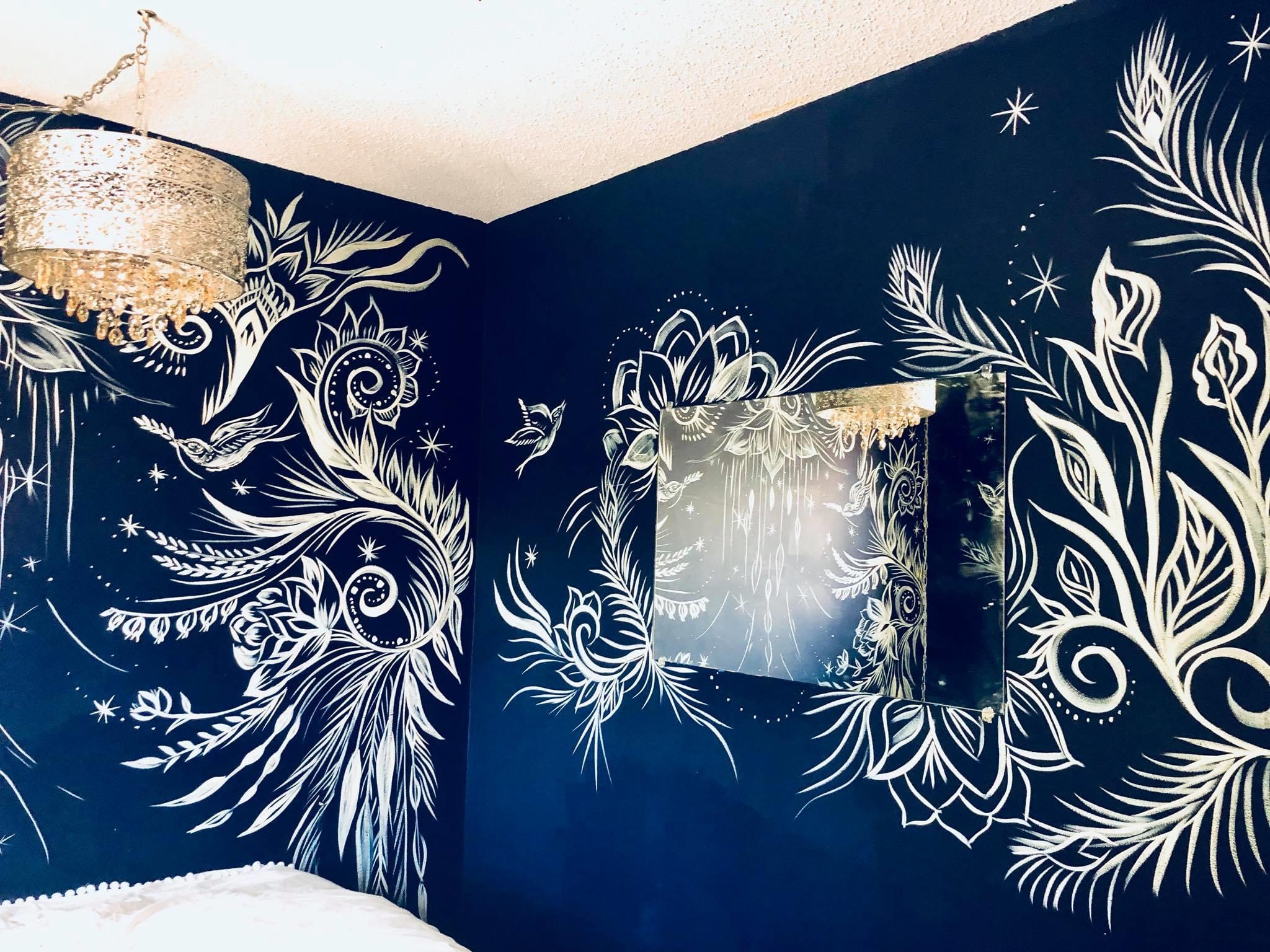 Dark blue wall with white floral and bird mural, mirror, and ceiling light fixture.