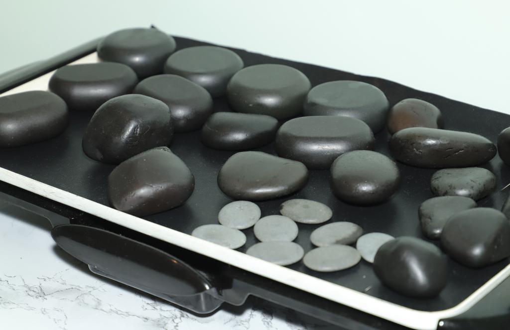 Flat device with smooth, rounded black stones and small white circular objects on its surface.