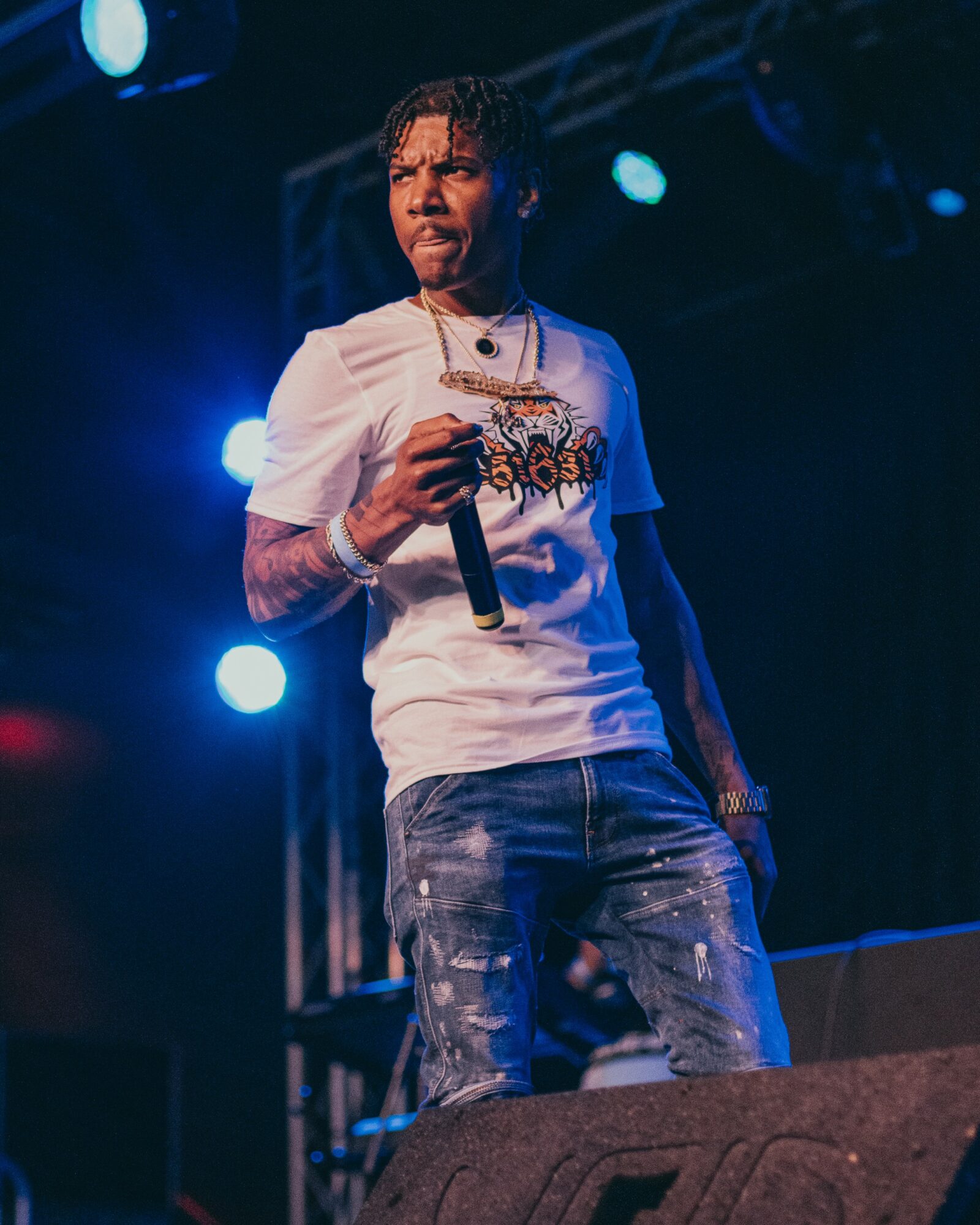 Performer holding microphone on stage with blue and white lights, wearing a white shirt and distressed jeans.