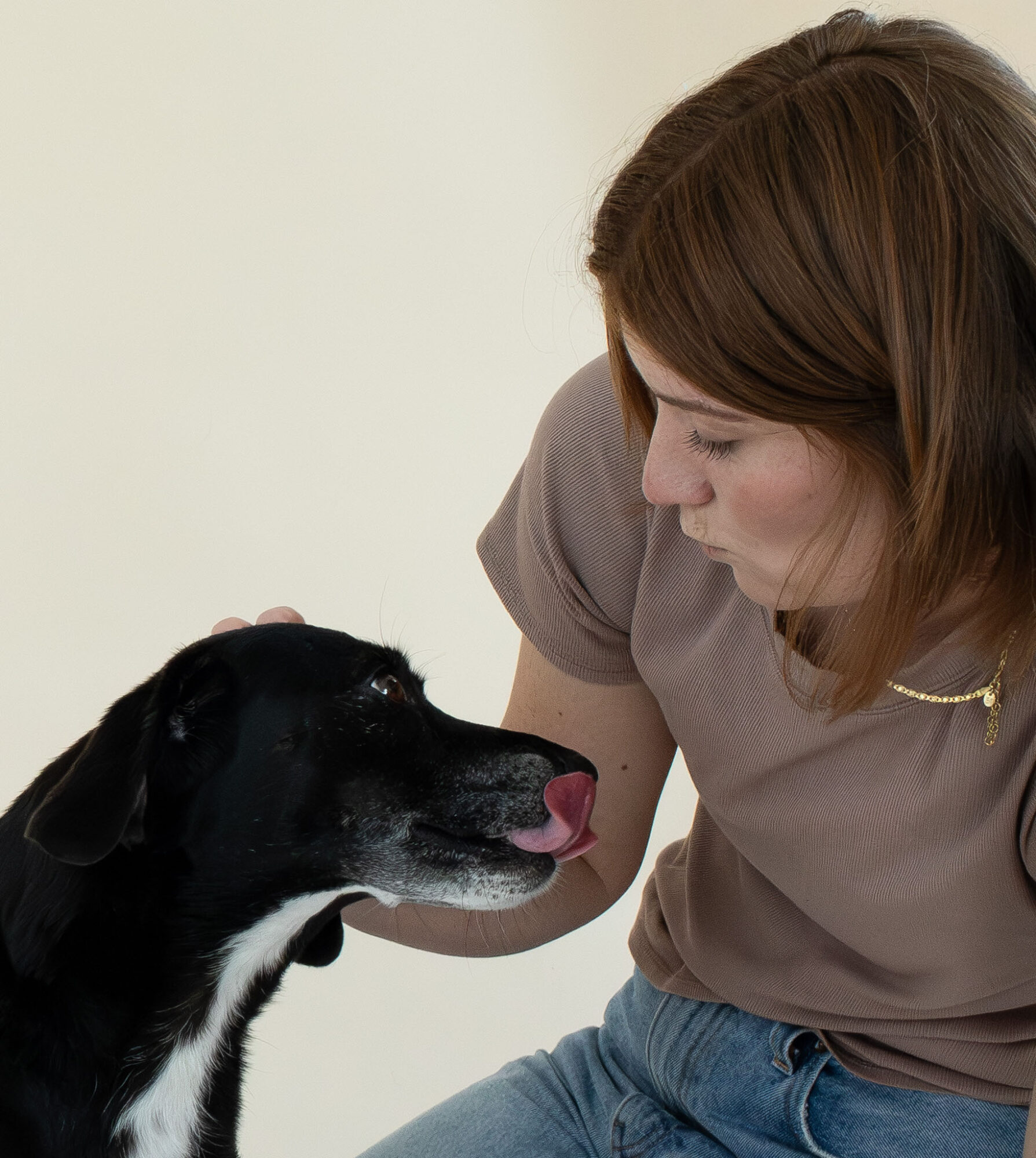 Woman with brown hair leaning toward a black and white dog, both with noses close, indoors.