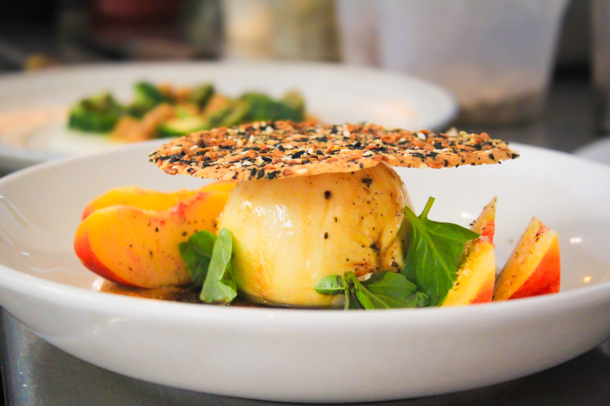 A plated dish with a large piece of fish, vegetables, and a crispy garnish on top, served in a white bowl.