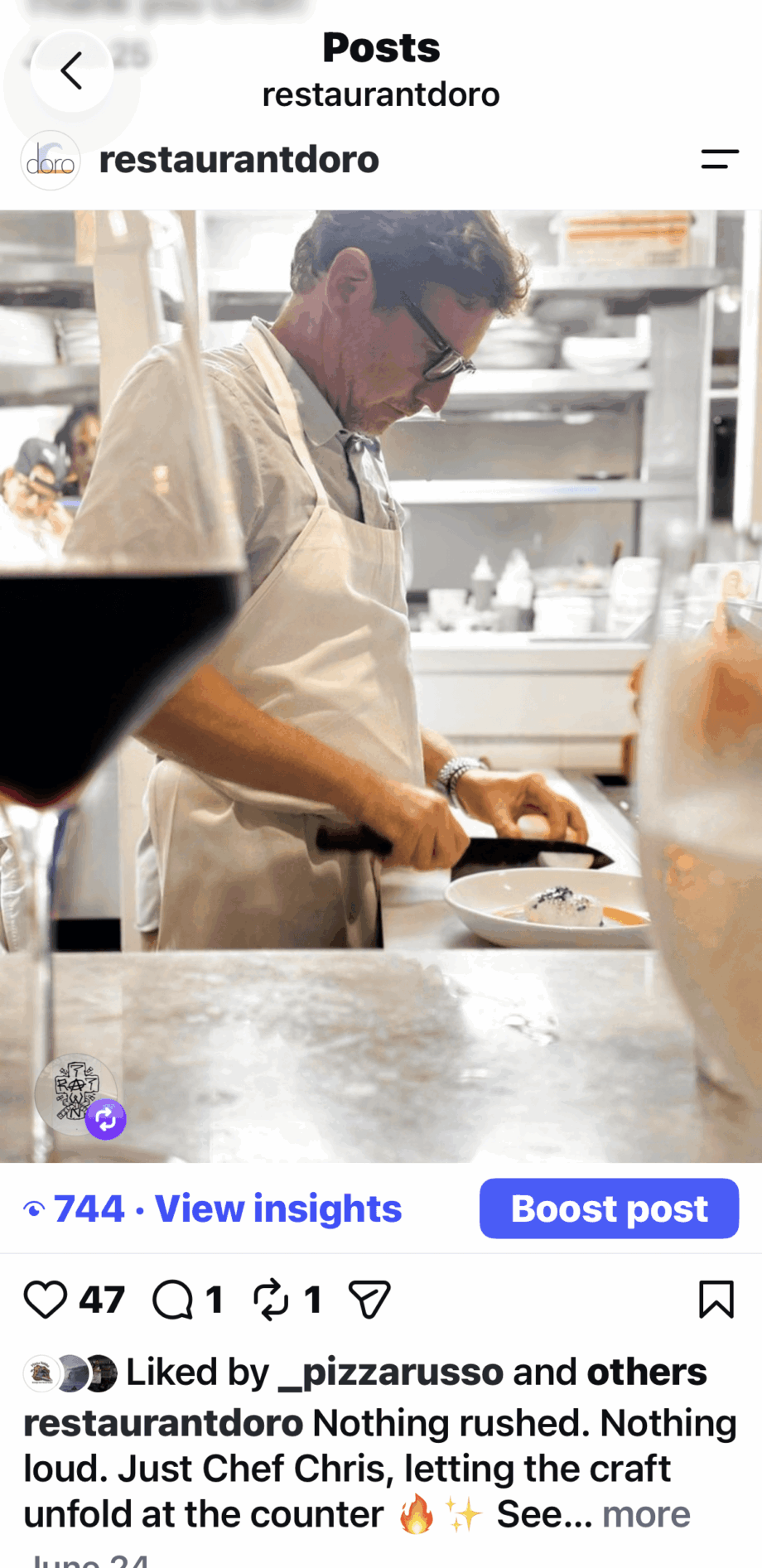 Chef preparing food in a restaurant kitchen with a glass of wine in the foreground.
