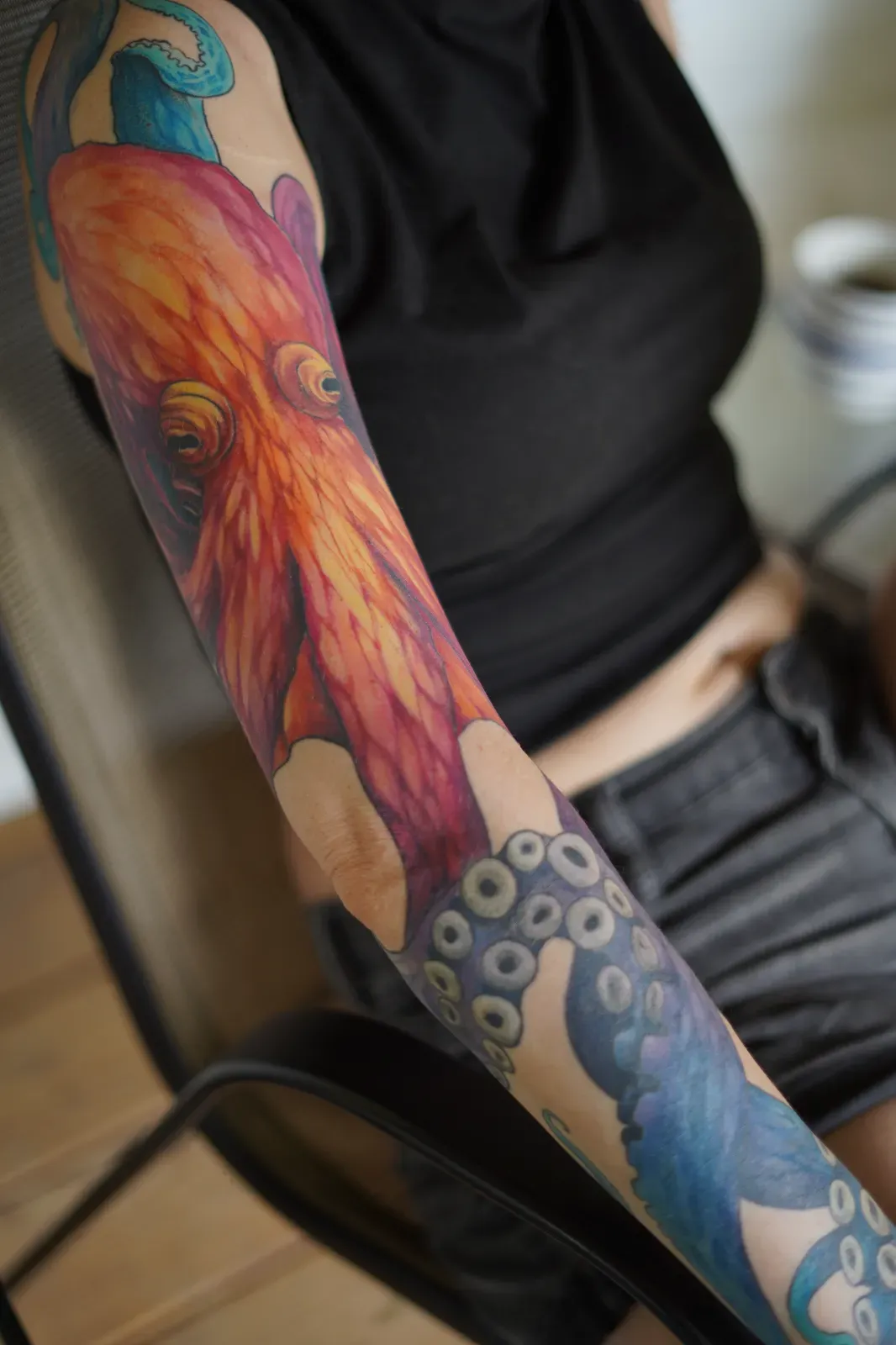 Colorful tattoo of a lion's face on a person's arm, with blue and gray patterns below, and part of a black shirt visible.