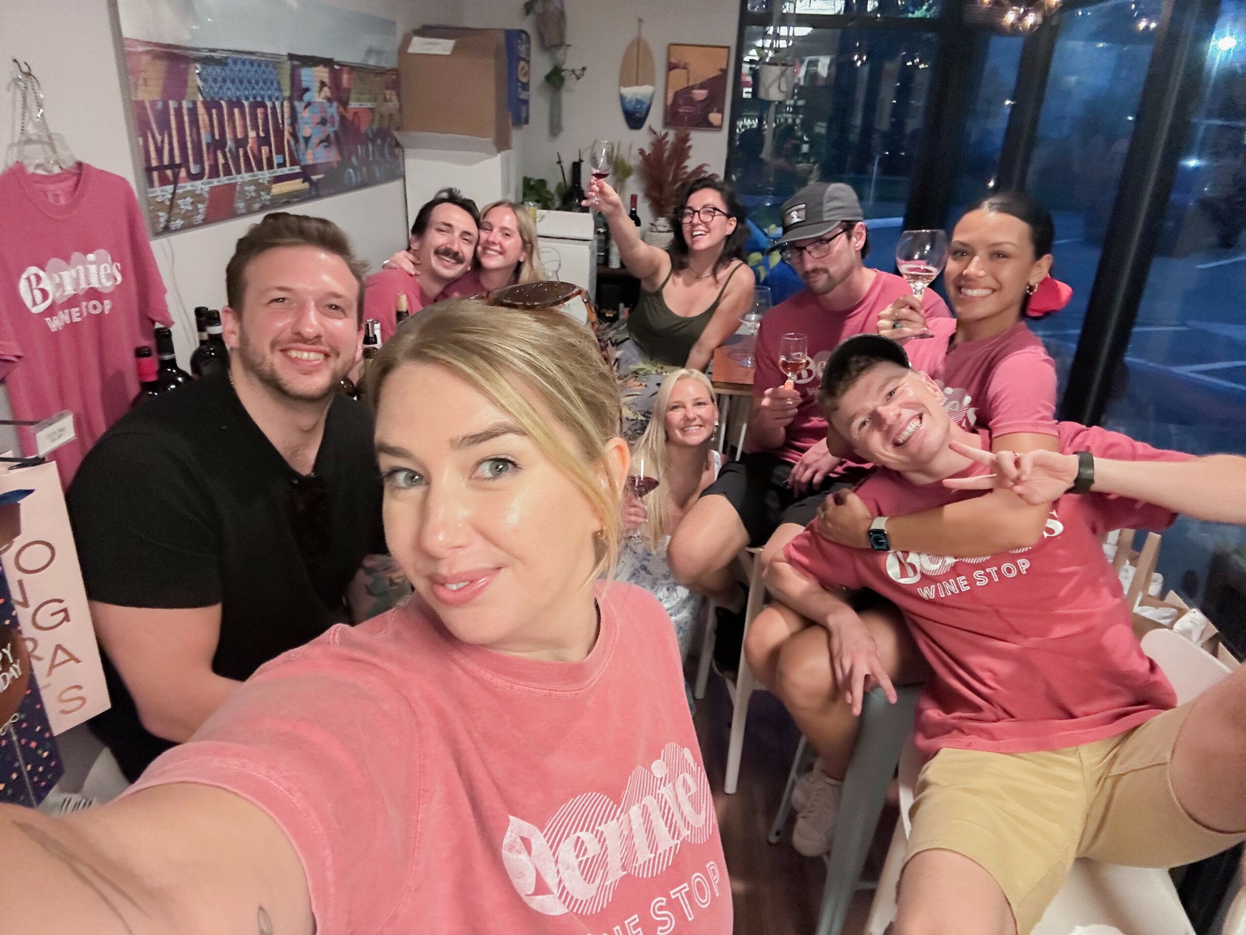 Group of friends smiling and posing for a selfie in a lively indoor setting with colorful decorations and large windows.