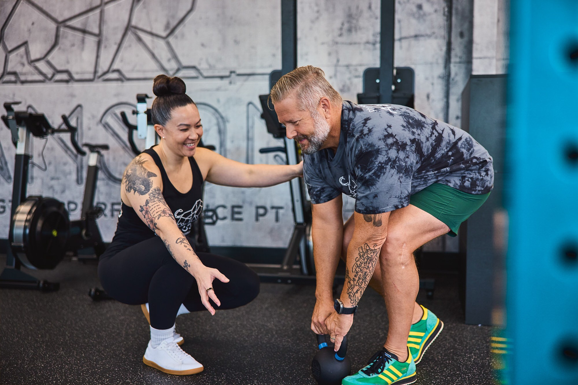 A woman and a man are in a gym, smiling and engaging in a workout together.
