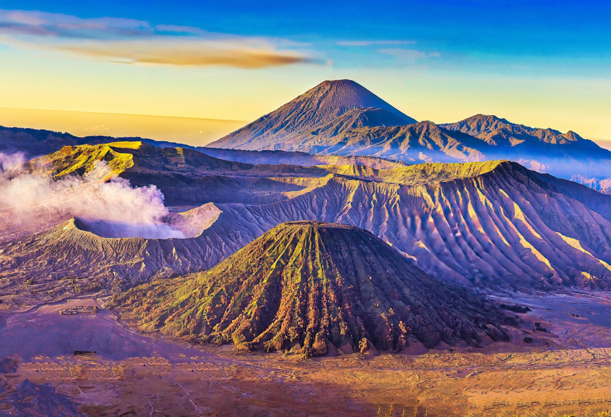 Volcanoes and mountains under a colorful sky, with clouds near the ground, in a scenic landscape.