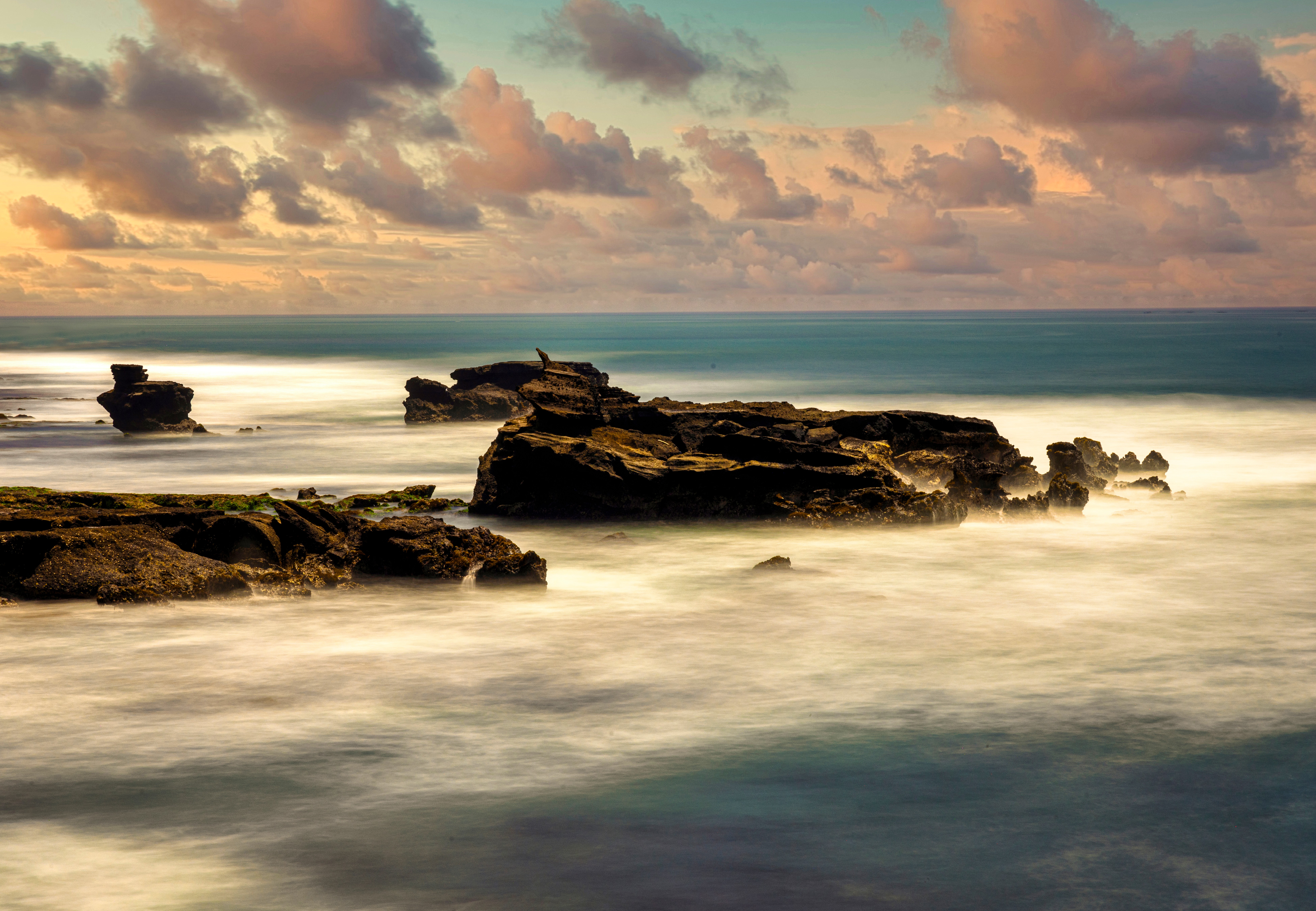 Seascape with rocks in water, cloudy sky, and sunset colors, long exposure effect on waves, horizon in distance