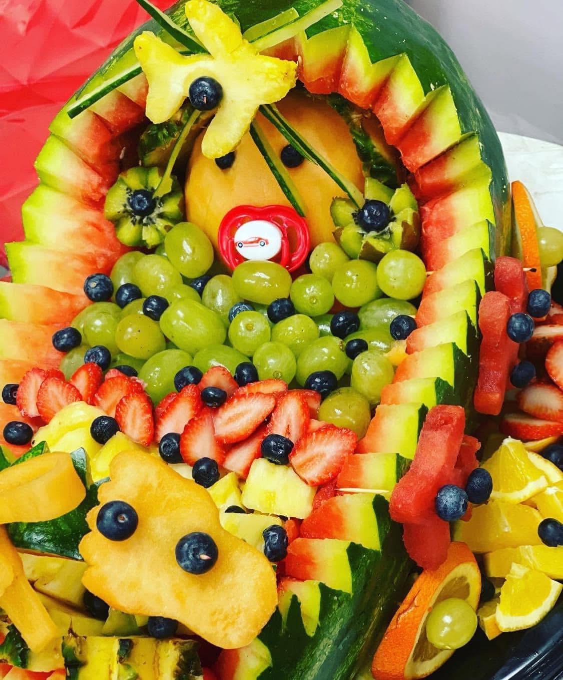 Colorful fruit arrangement with watermelon, pineapple, grapes, strawberries, and blueberries, decorated with carved fruit and edible flowers.