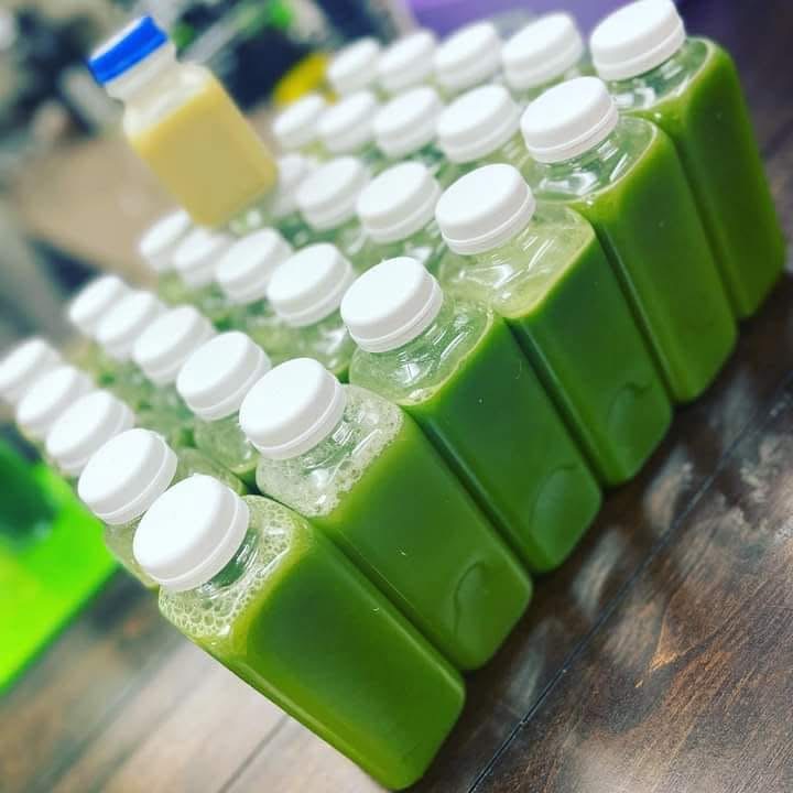 Multiple bottles filled with green liquid arranged on a wooden surface, with a blurred background of other bottles and containers.