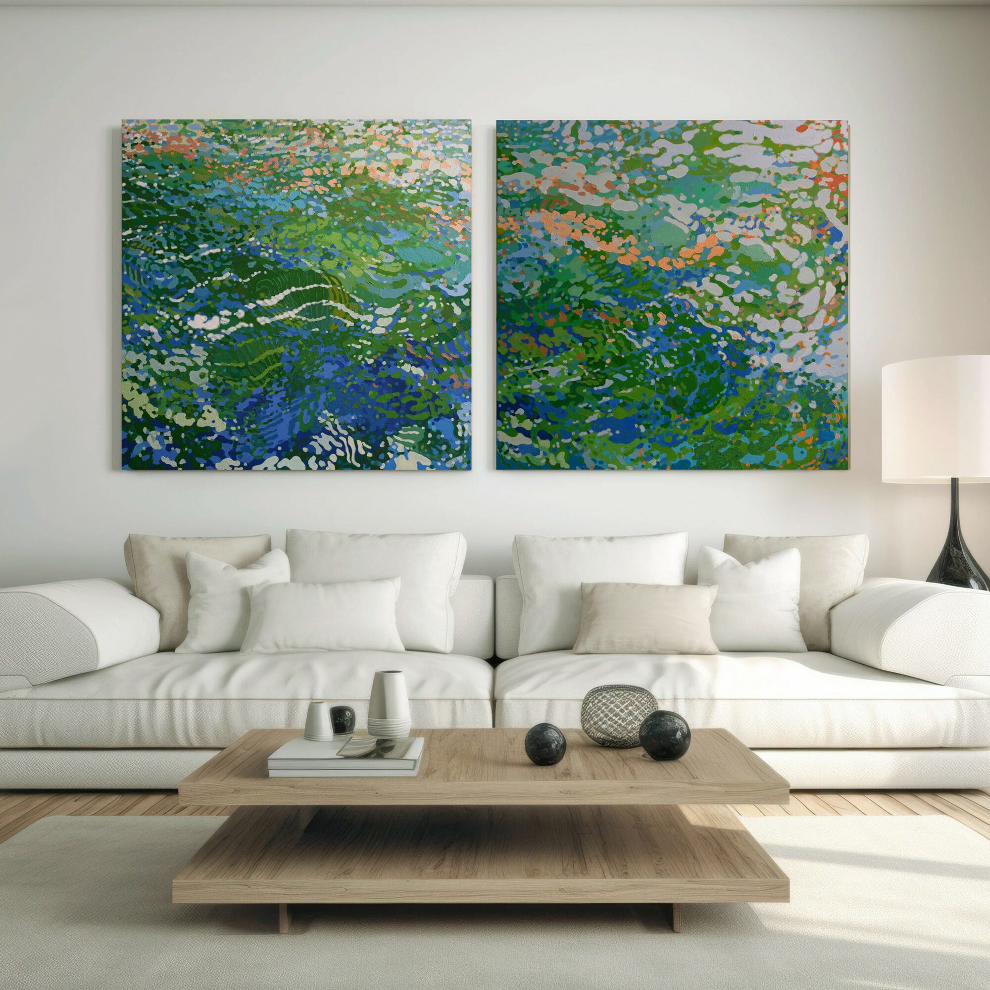 Two abstract landscape paintings hang above a white sofa in a modern living room, with a wooden coffee table and a white lamp.